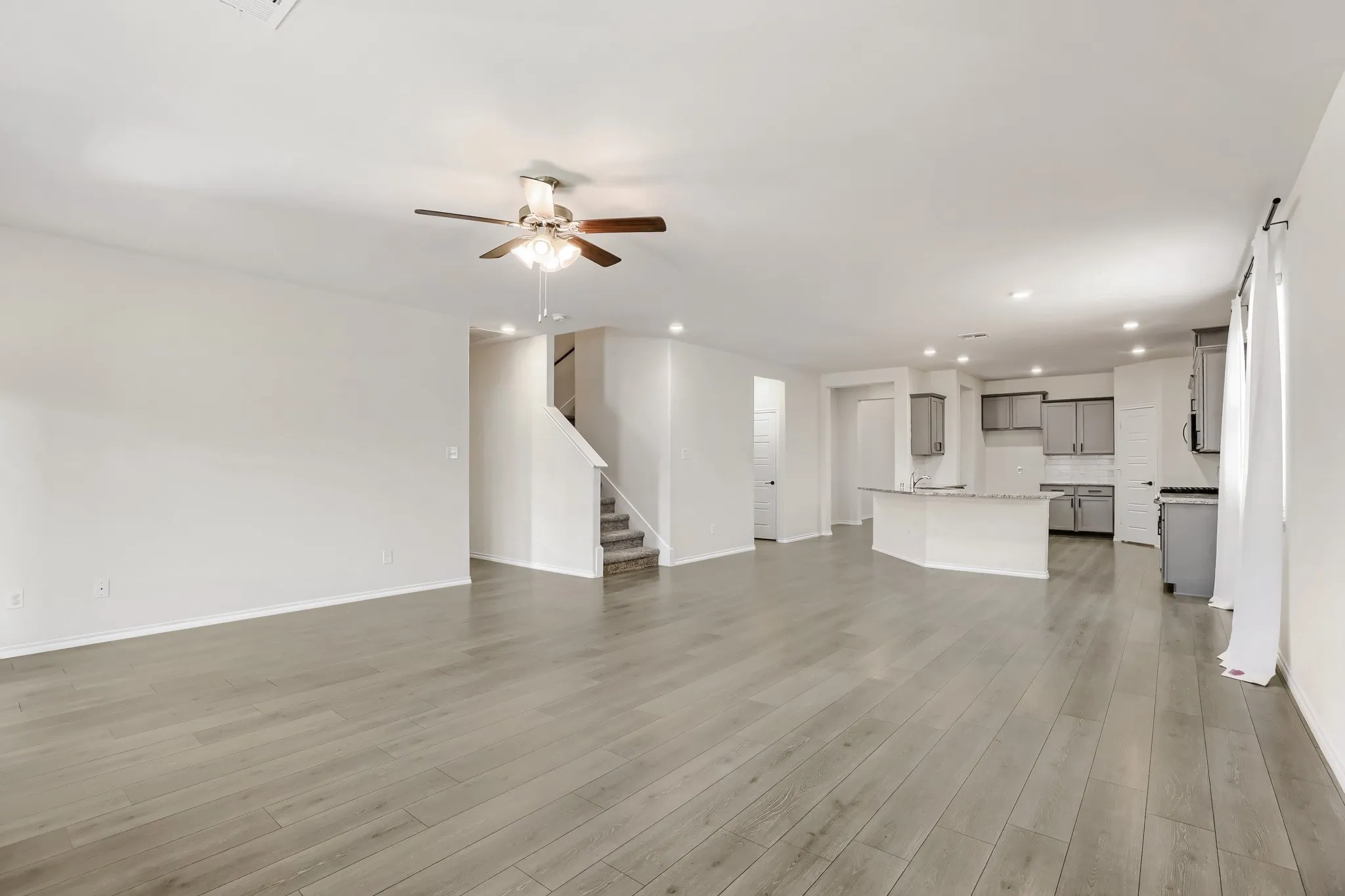 Spacious open-concept interior with wood-finish flooring, recessed lighting, and a ceiling fan