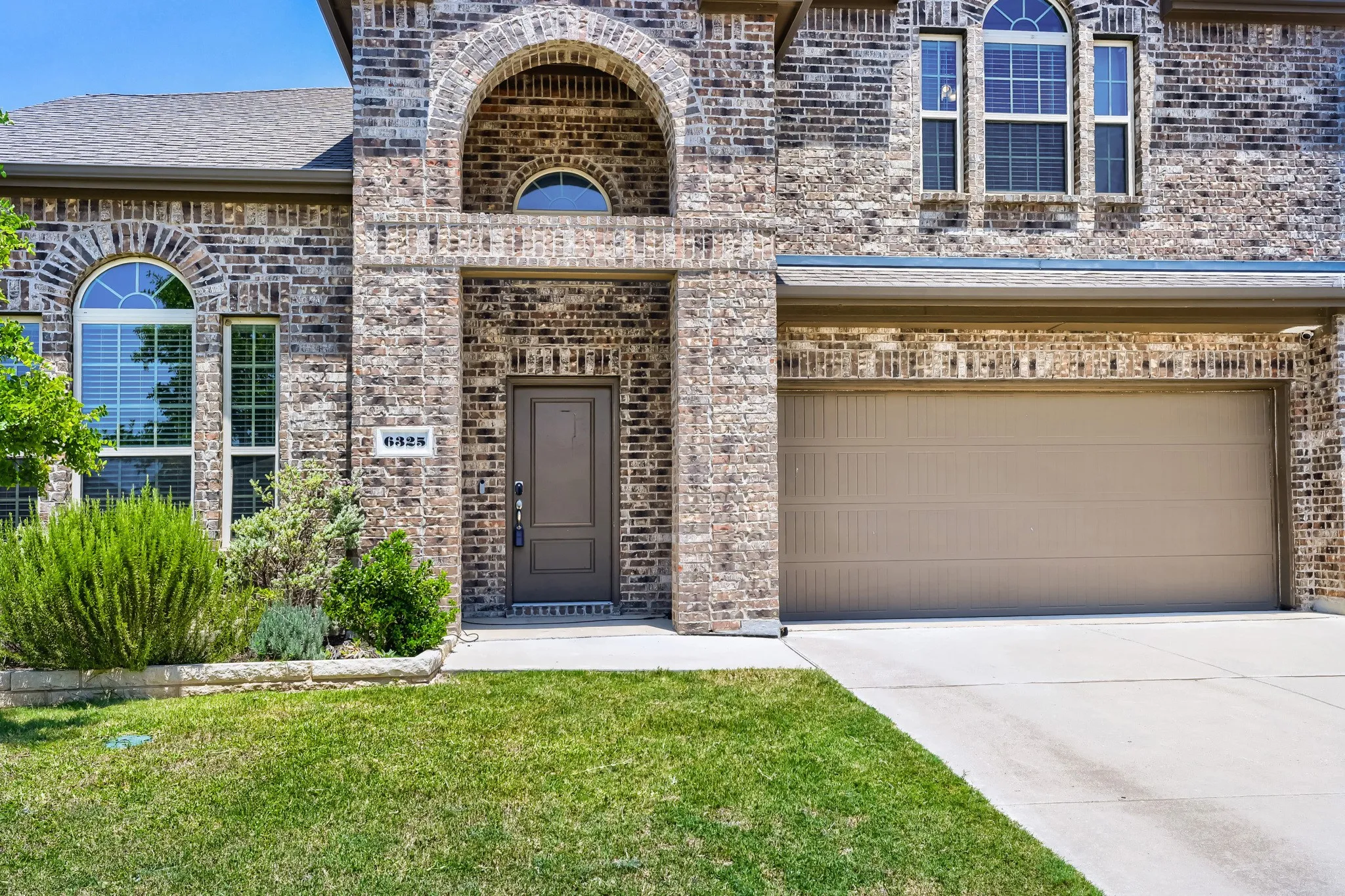 Brick exterior with arched entryways, integrated garage, and a manicured lawn