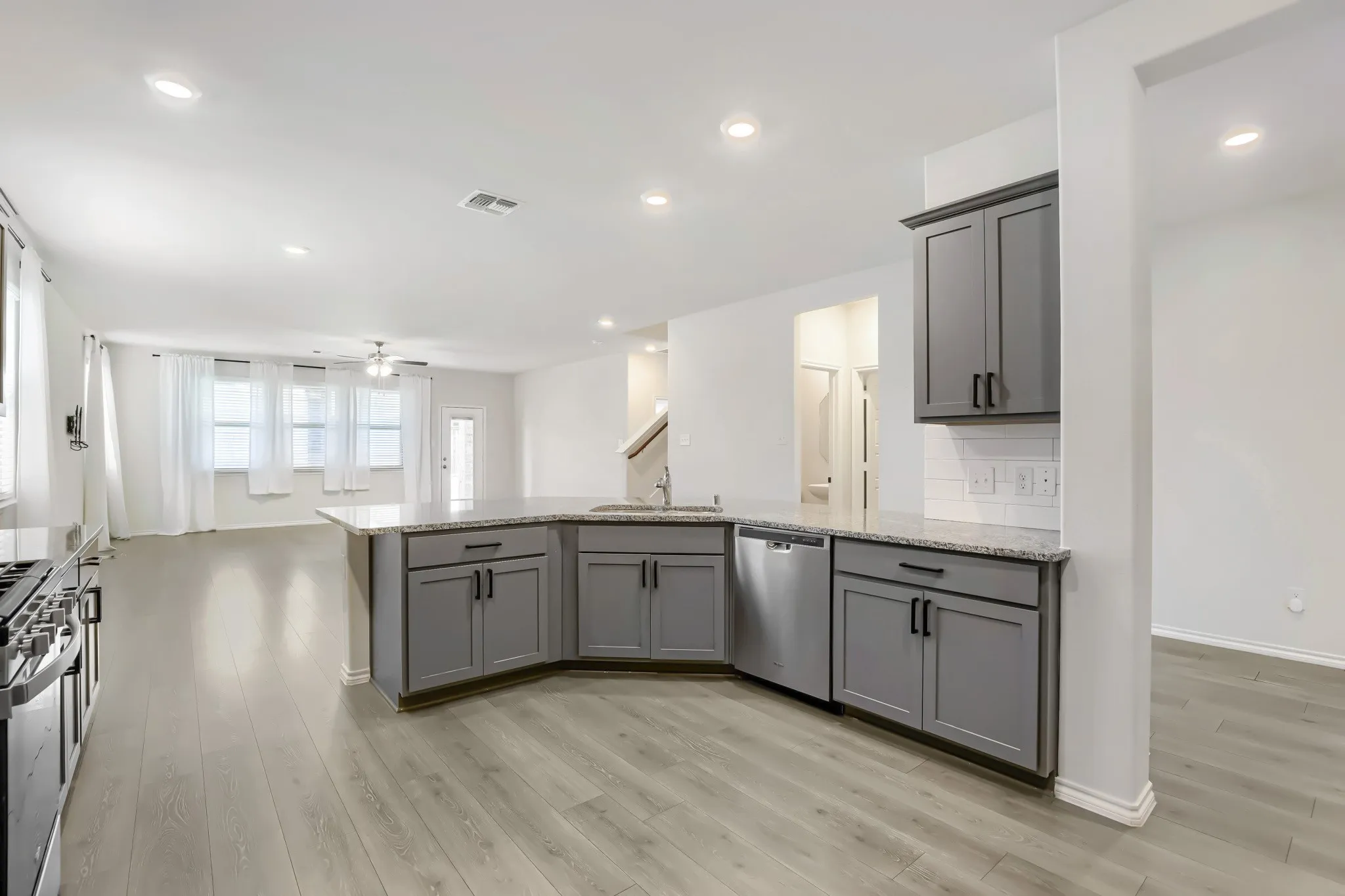 Open-concept kitchen with wood-finish flooring, gray cabinetry, stainless steel appliances, and recessed lighting