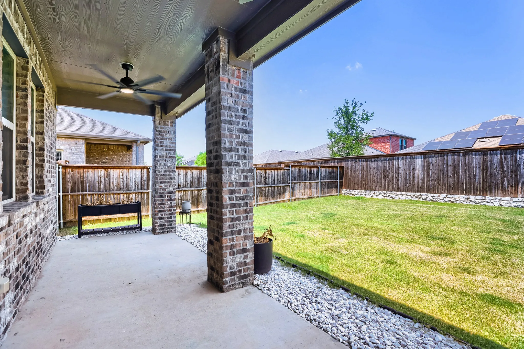 Covered outdoor patio with a ceiling fan, concrete flooring, brick columns, and a grassy backyard area