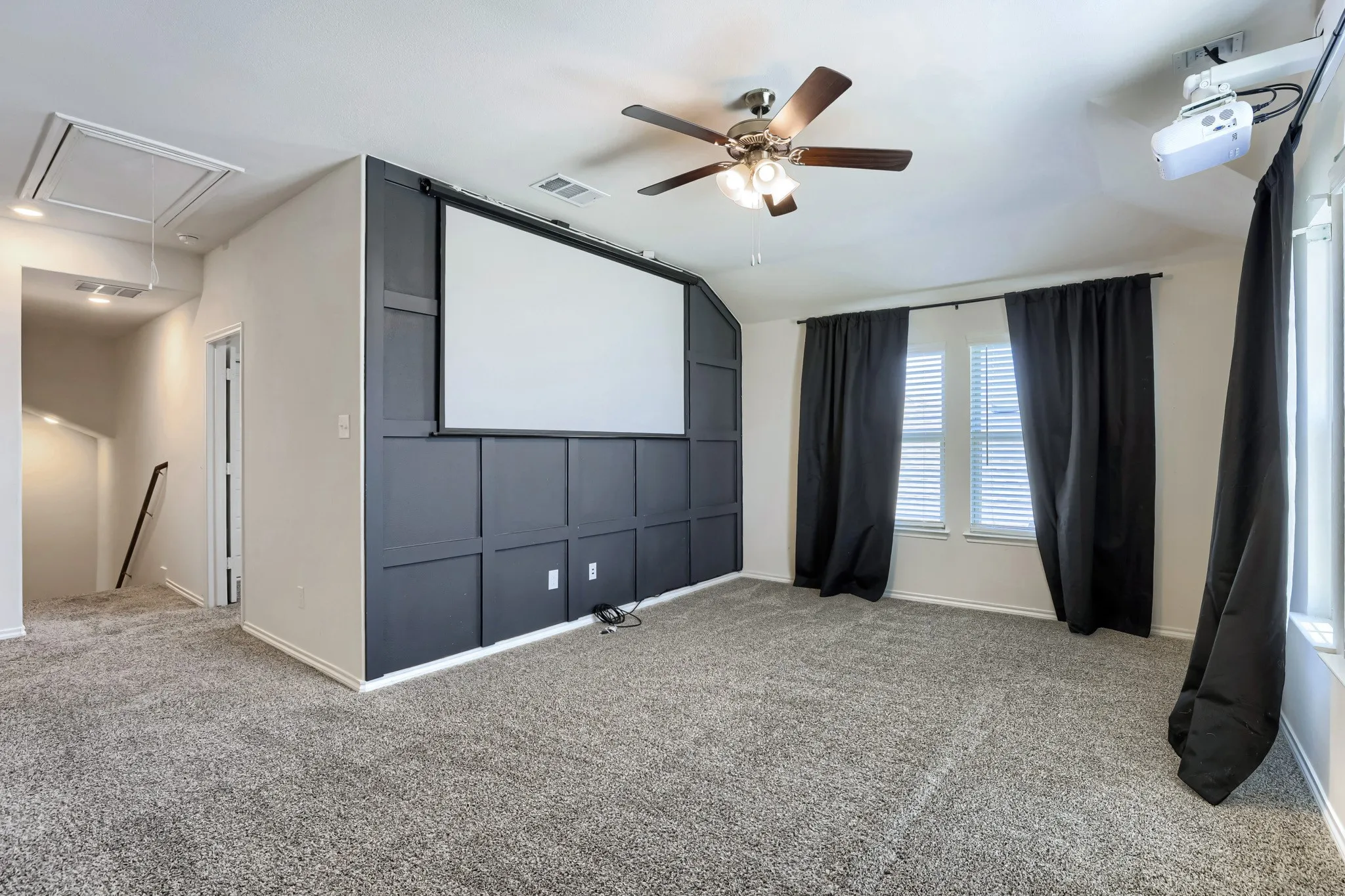Carpeted room featuring a ceiling fan, built-in projector, projection screen, and window treatments