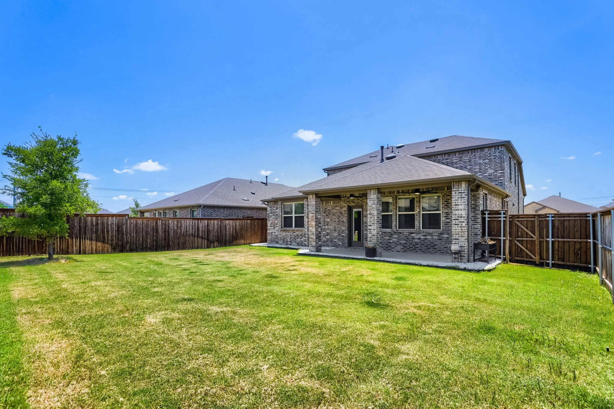 Expansive backyard with a manicured lawn, full privacy fencing, and a covered patio with brick columns