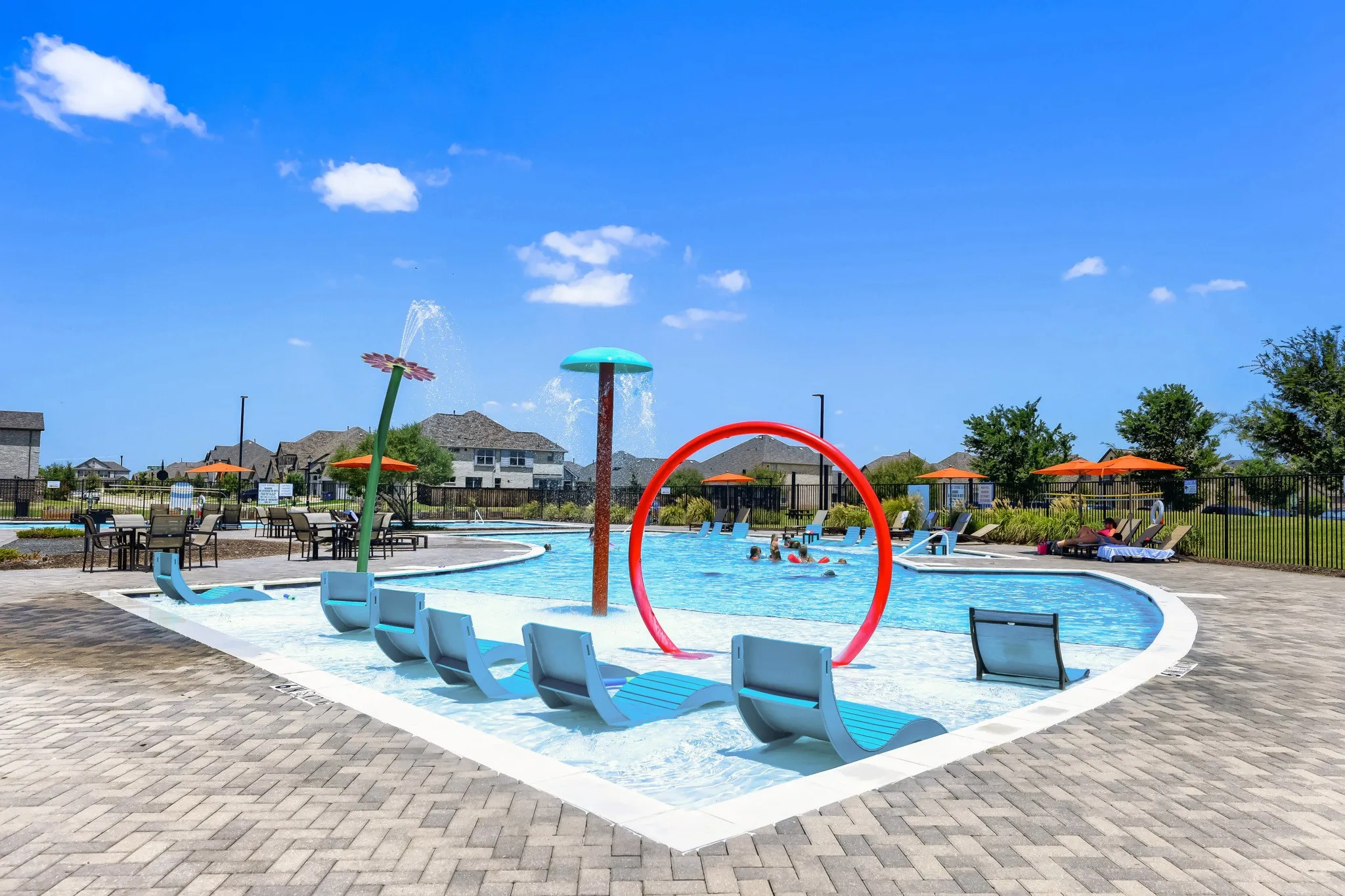 Resort-style pool with water features, integrated in-pool lounge seating, surrounding paver decking, and dedicated splash pad areas