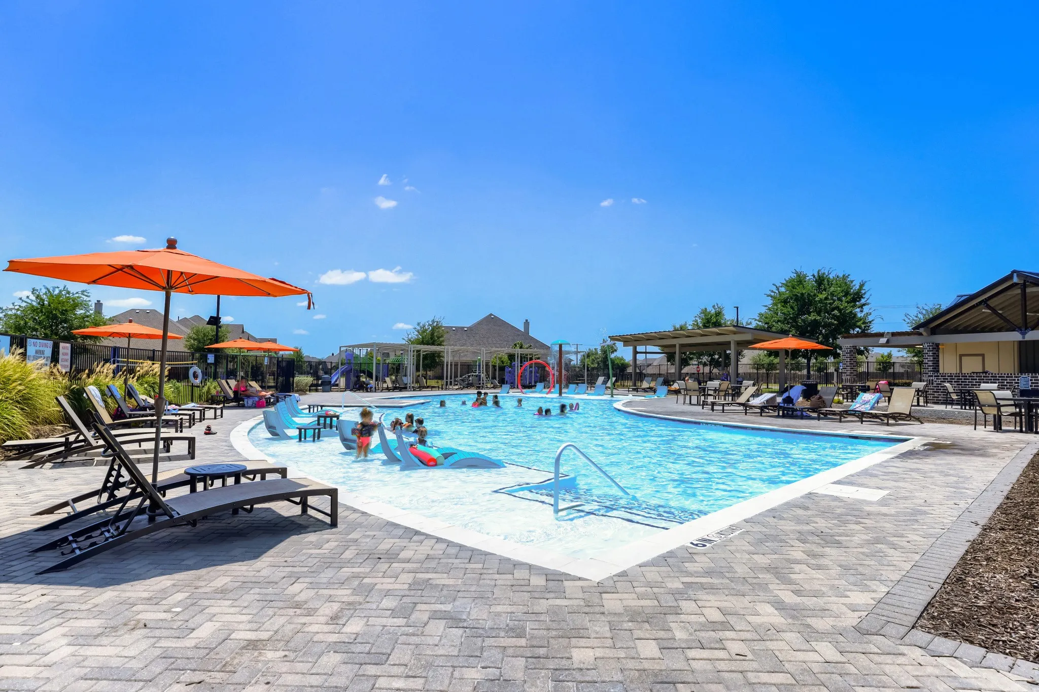 Expansive community pool with a sun shelf, paved lounging areas, and shaded pergolas