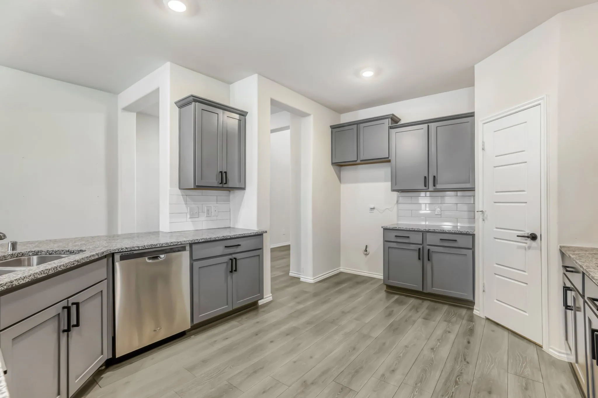 Gray cabinetry with black hardware, stainless steel dishwasher, white subway tile backsplash, light wood-finish flooring, and recessed lighting