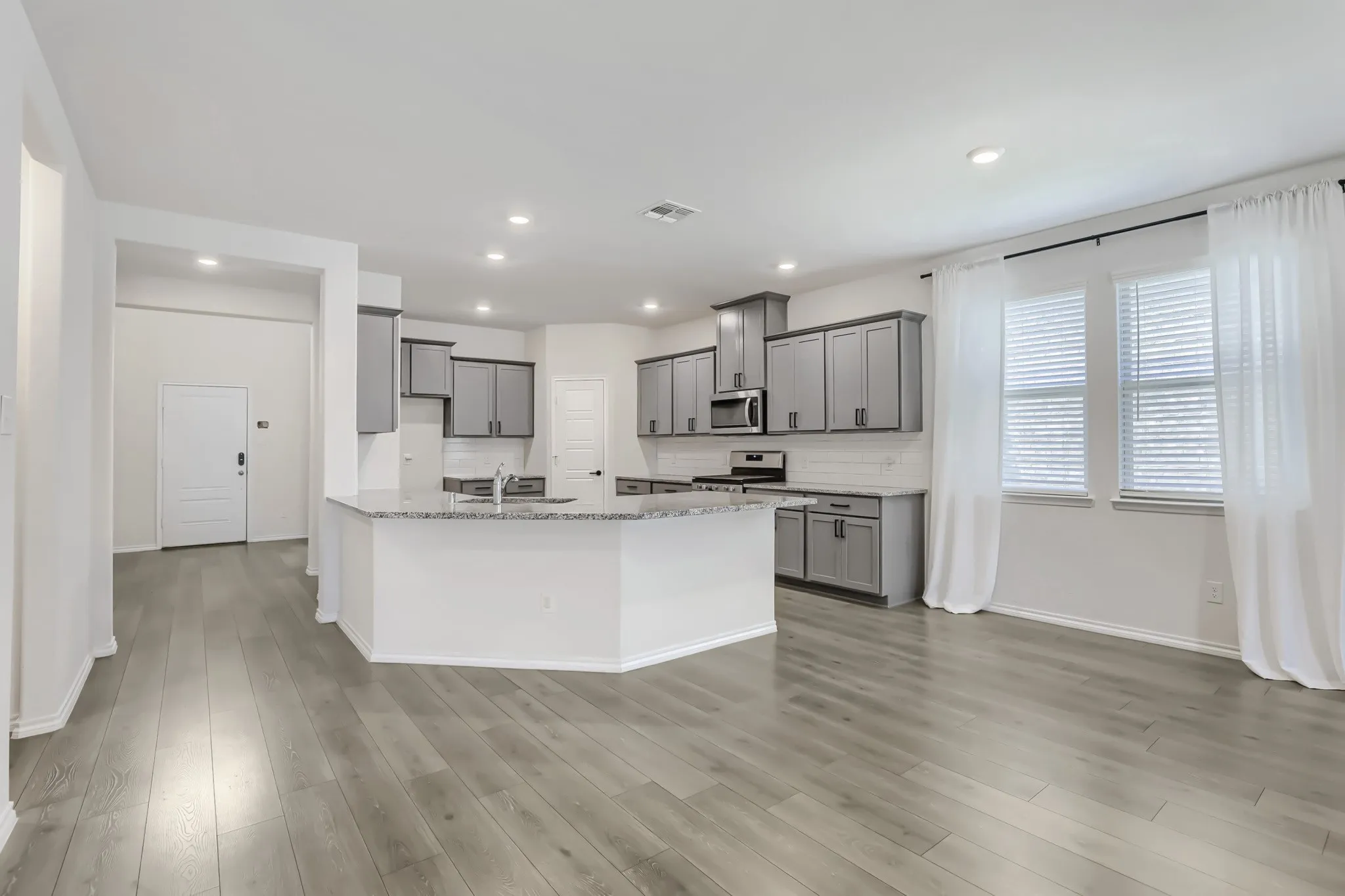 Open-concept kitchen featuring an expansive island, grey cabinetry, stainless steel appliances, and wood-finish flooring