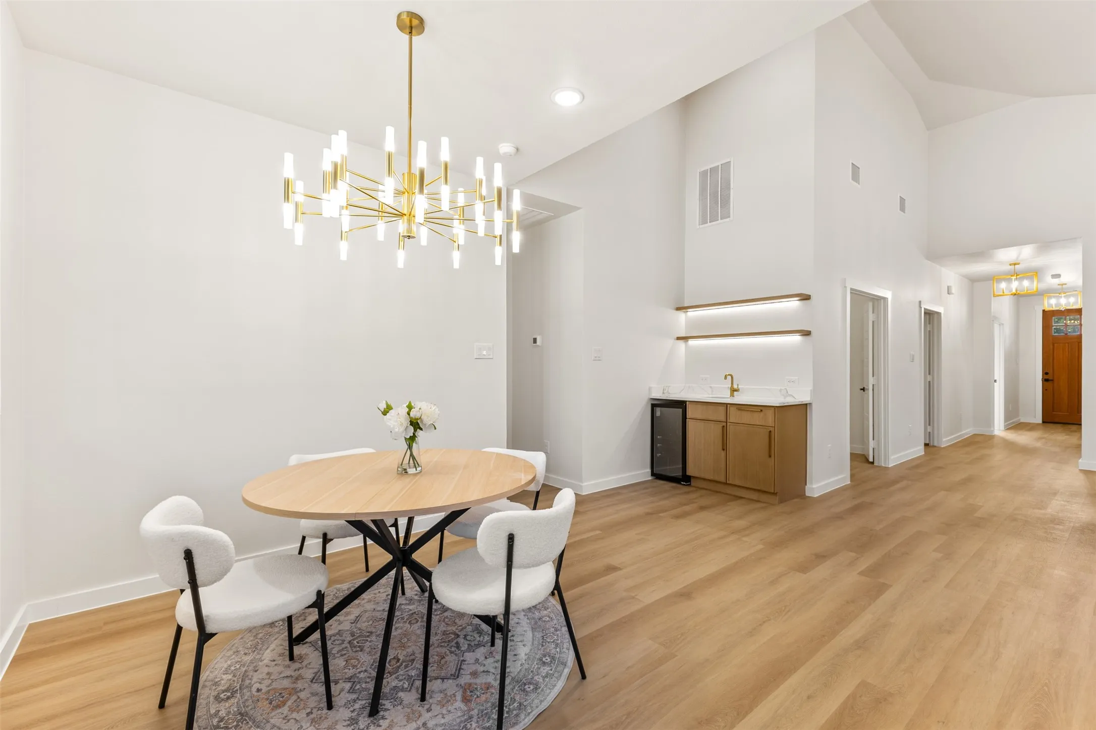 Spacious interior featuring a contemporary gold-finish chandelier, vaulted ceilings, and light wood-finish flooring