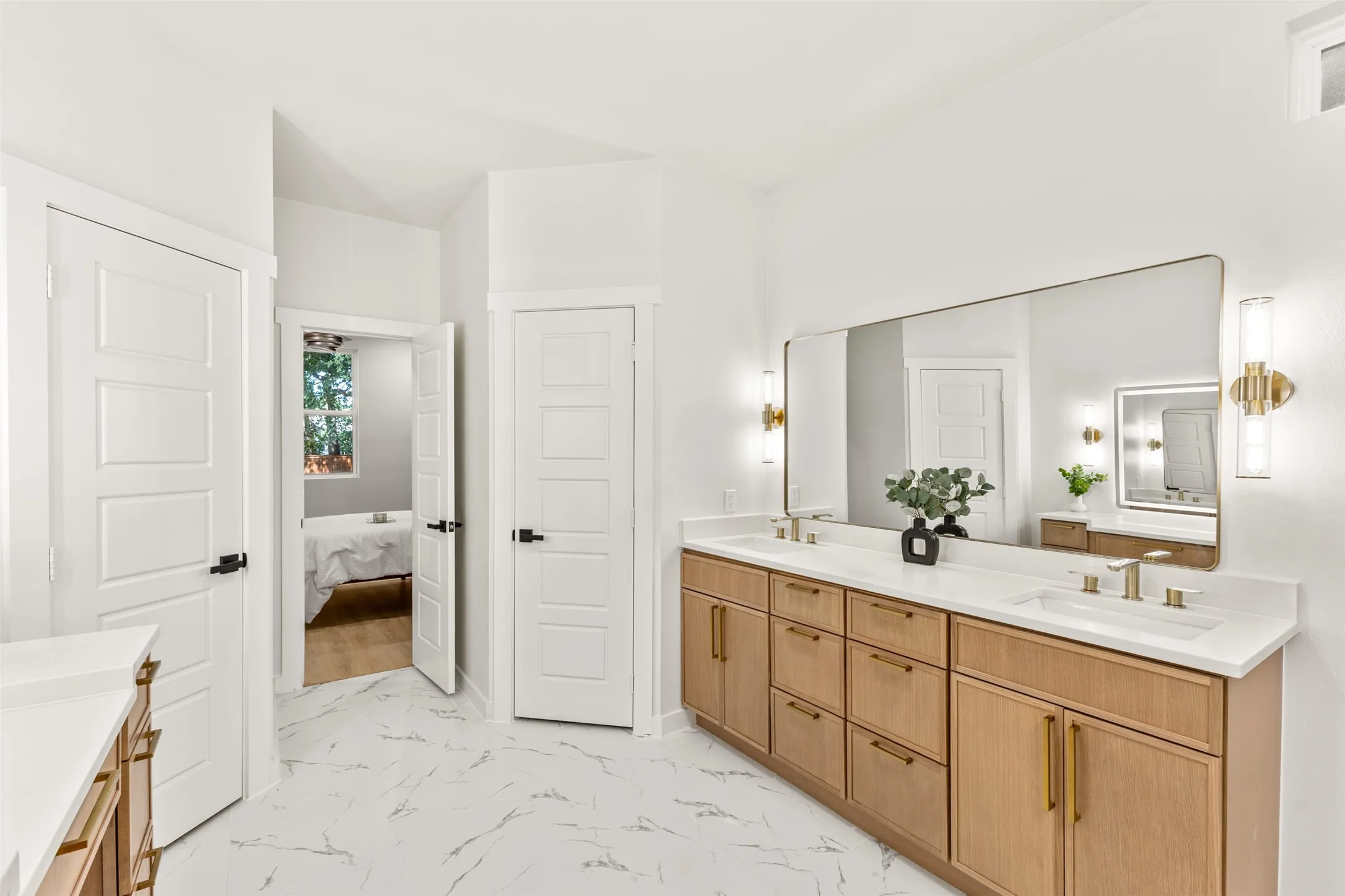 Spacious bathroom featuring a dual vanity with light wood cabinetry, white countertops, and gold-finish hardware