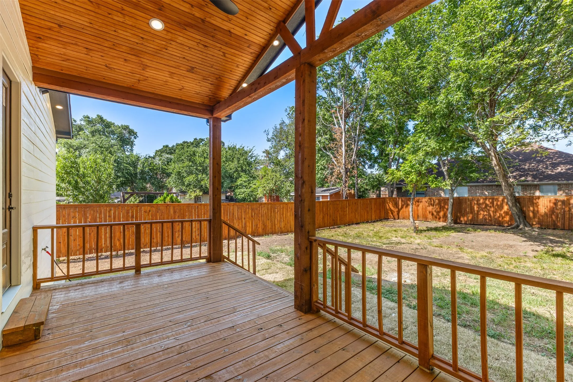 Covered outdoor deck with stained wood flooring, exposed beam ceiling with recessed lighting, and a dark-toned ceiling fan