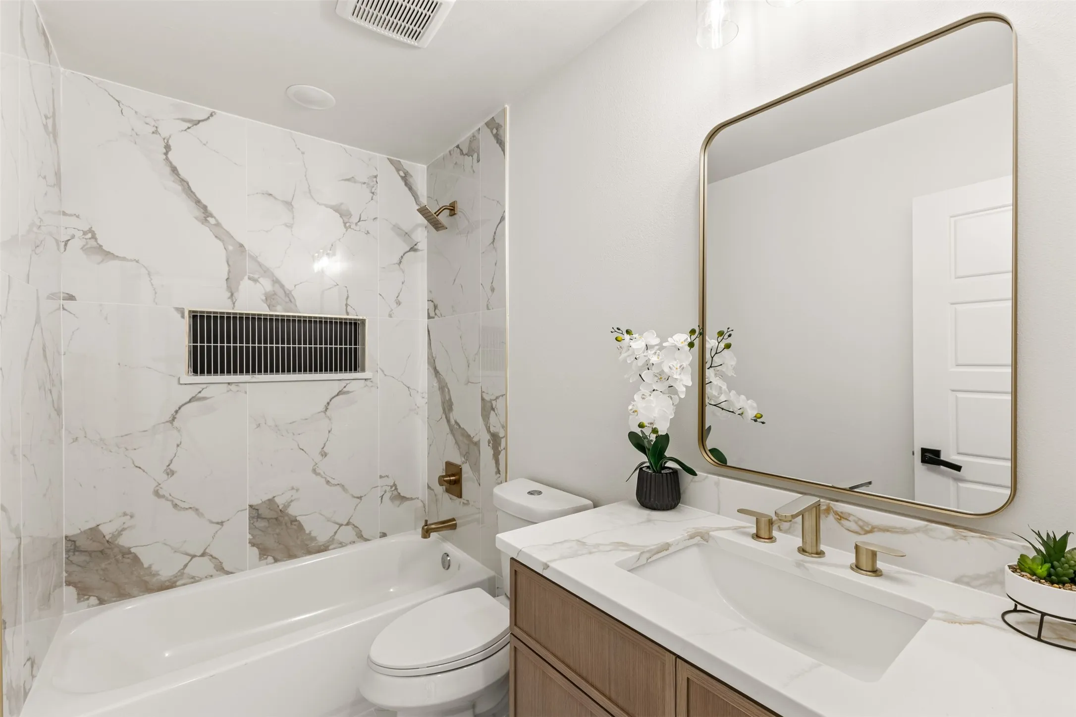 Bathroom featuring a white bathtub, marble-patterned tile shower surround, and gold-toned fixtures
