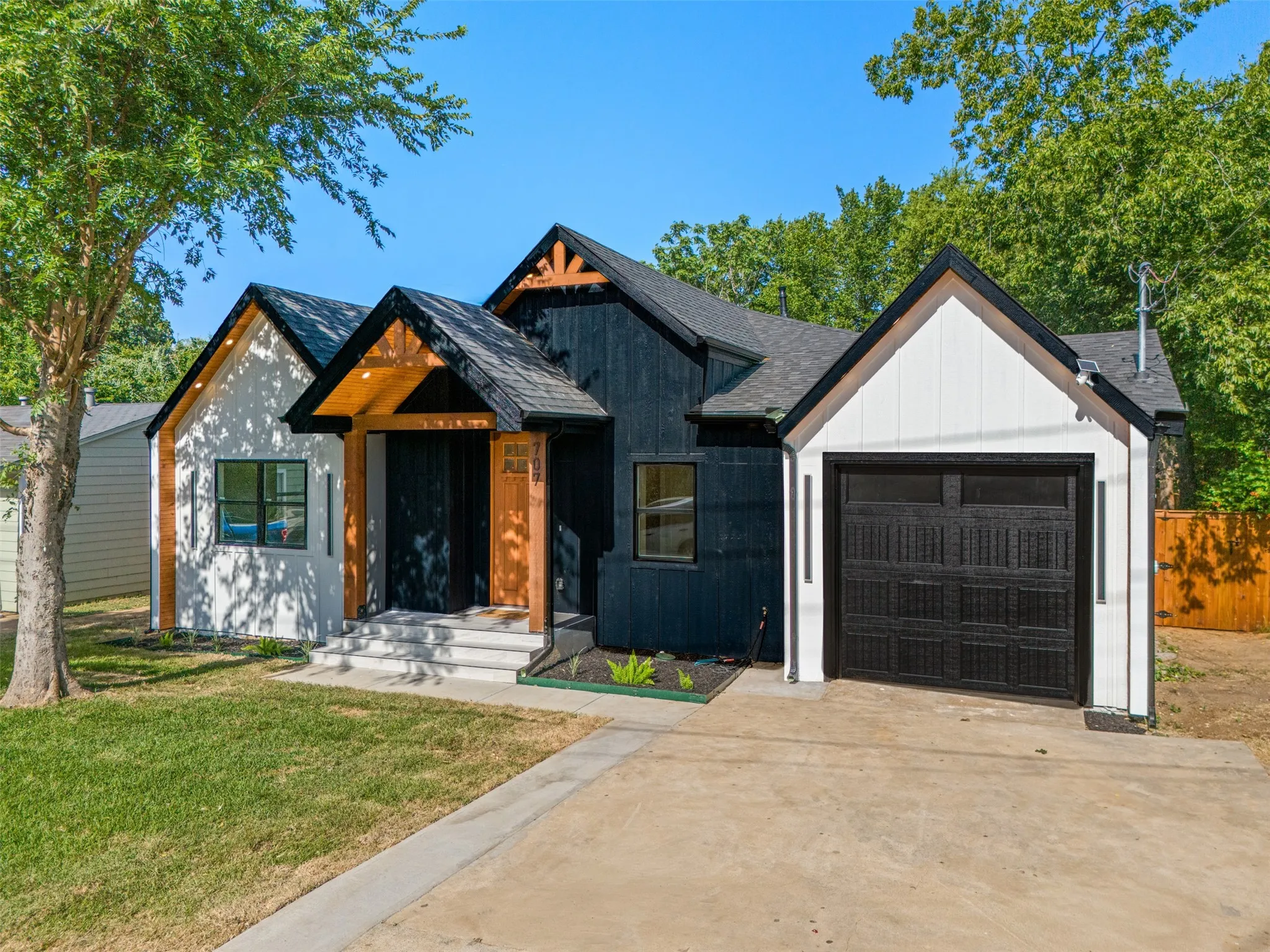 Modern farmhouse exterior featuring black and white siding, a single-car garage, a covered entry with exposed wood beams, and a concrete driveway