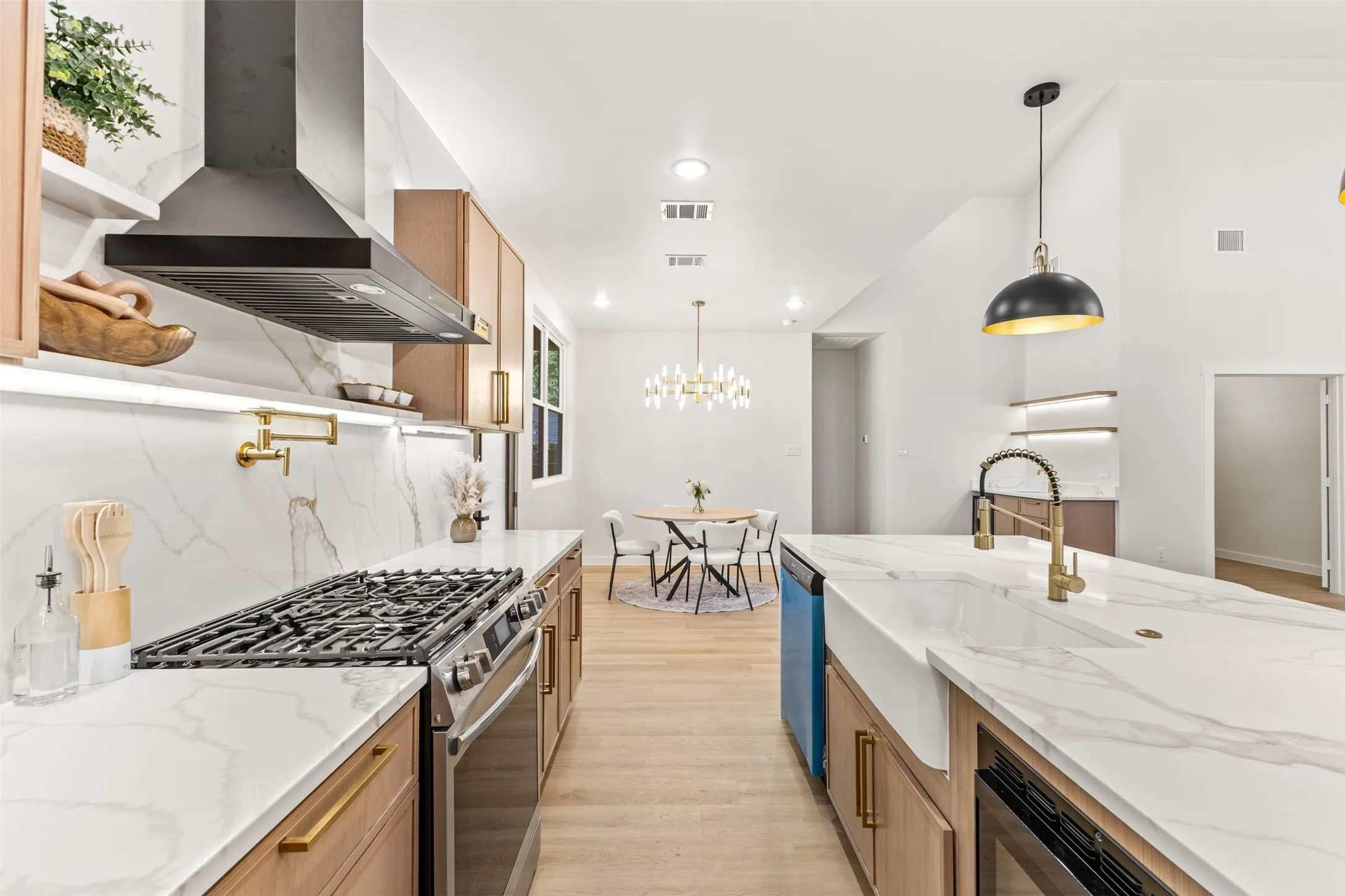 Open-concept kitchen featuring marble-finish countertops, natural wood-finish cabinetry, a stainless steel gas range, a pot filler faucet, and a farmhouse sink