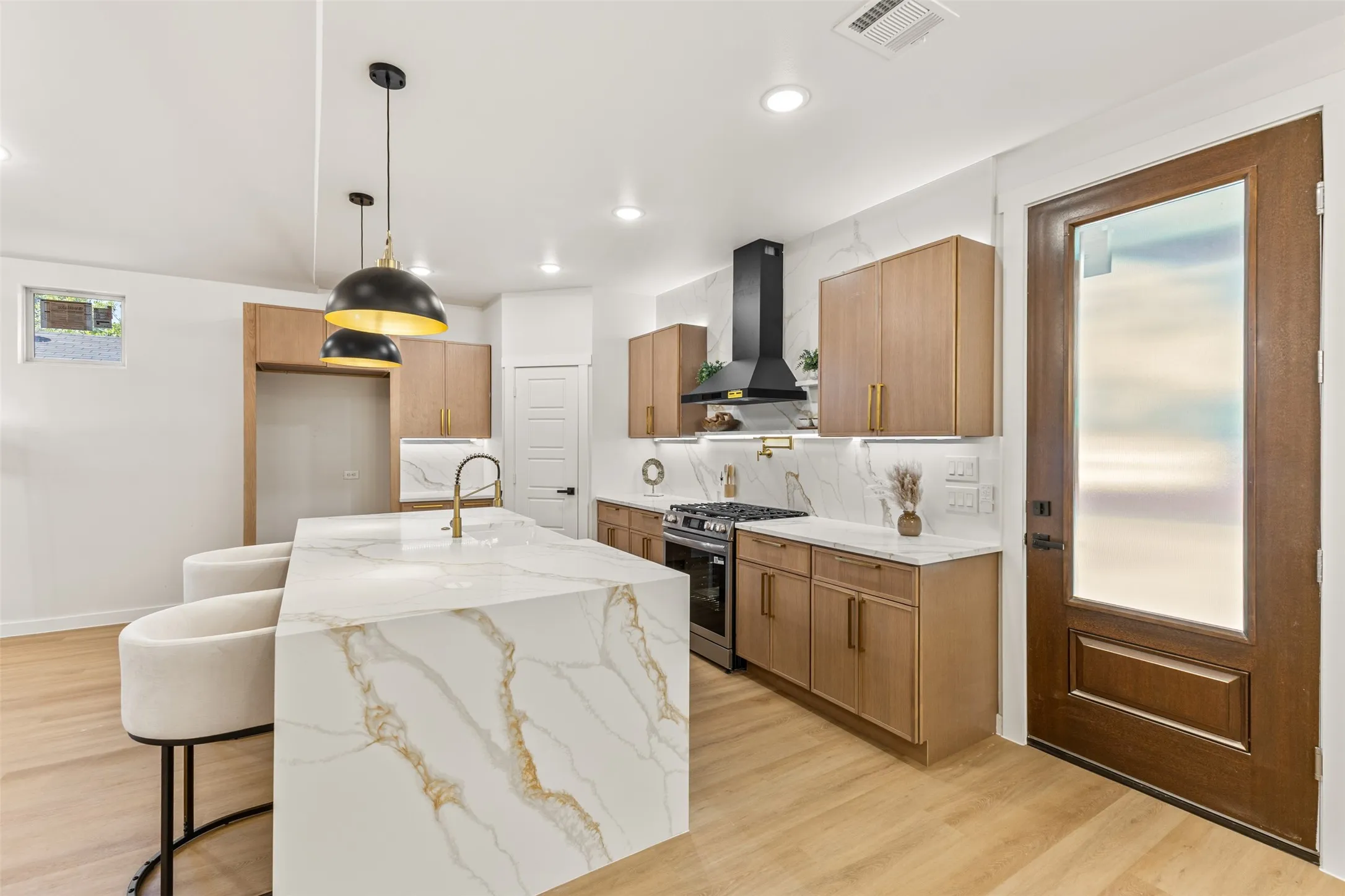 Contemporary kitchen featuring an oversized island with waterfall countertop, gold veining, and integrated sink