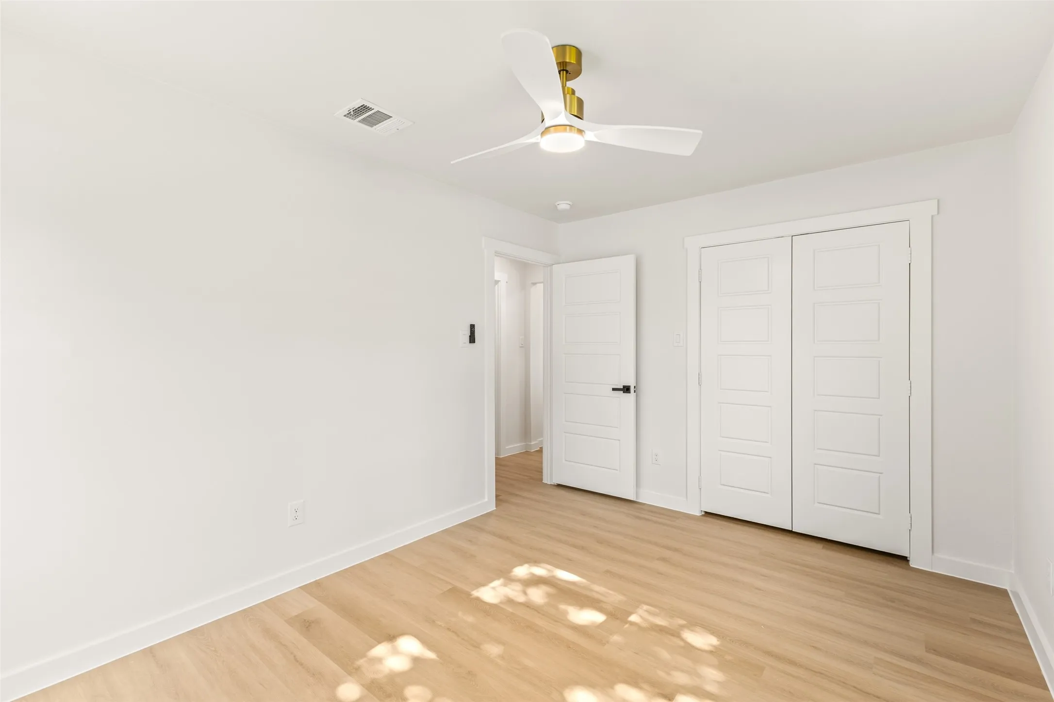 Room featuring wood-finish flooring and a white ceiling fan with a brass accent