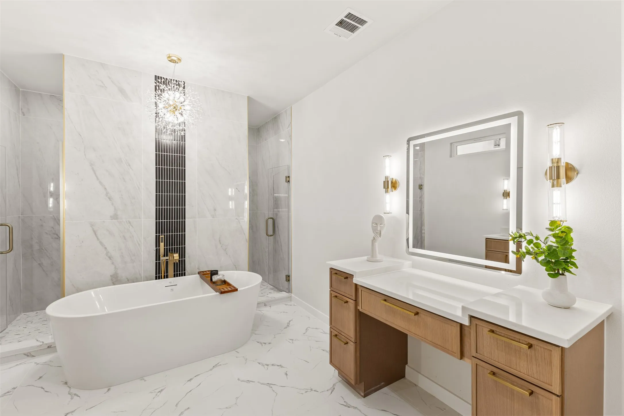 Freestanding soaking tub with brass fixtures, marble-look tile flooring, and marble-look wall tiling with an accent mosaic