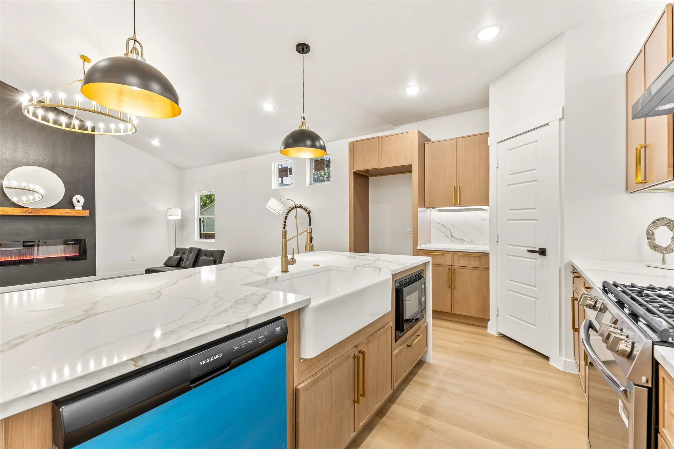 Open-concept kitchen featuring light wood-finish cabinetry, a large center island with a farmhouse sink and integrated microwave, and wood-finish flooring