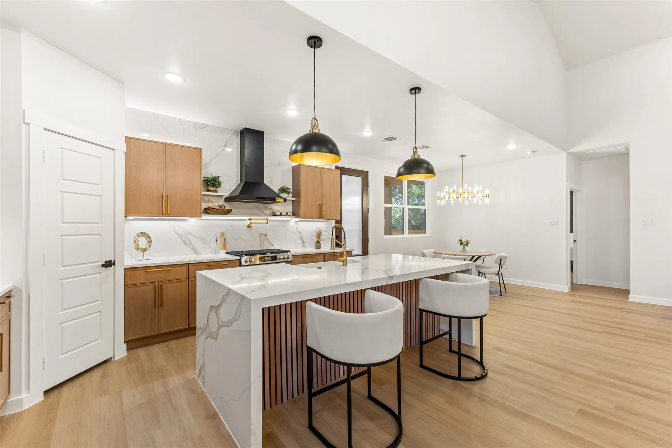 Contemporary kitchen featuring a waterfall island, light wood-finish flooring, and white marble-look countertops with coordinating backsplash