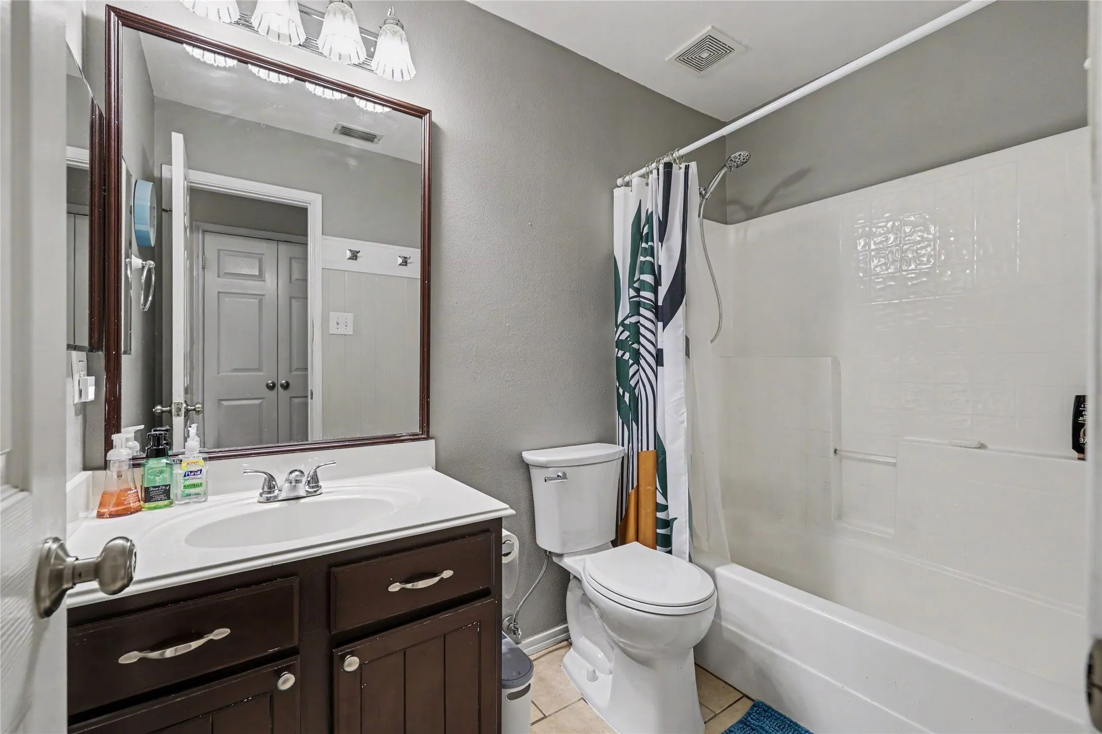 Bathroom featuring a white vanity top with an integrated sink, a dark wood-finish vanity cabinet, a framed mirror with overhead lighting, a toilet, and a white tub/shower combination with textured surround