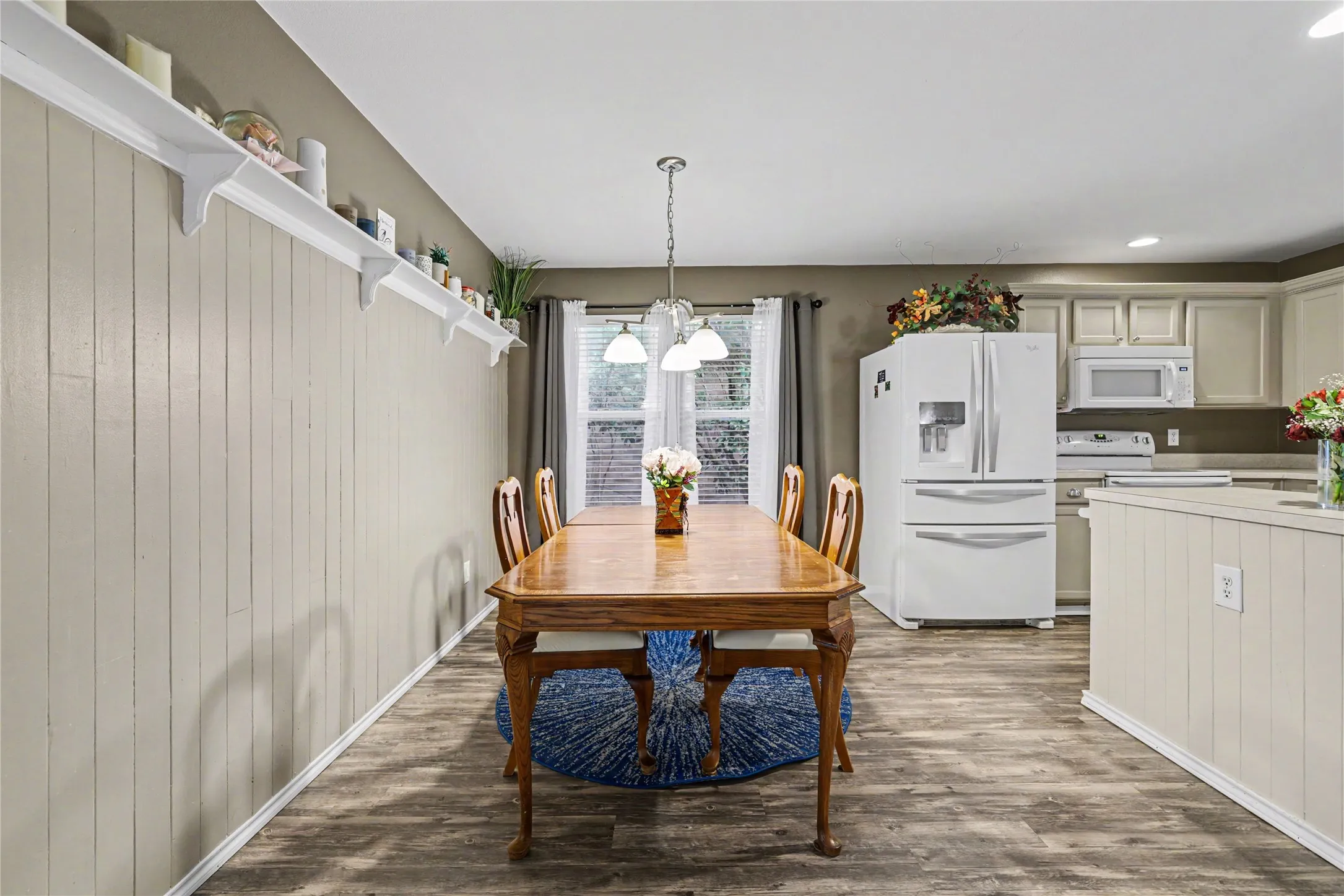 Spacious dining area featuring wood-finish flooring, white paneled wainscoting, and an open layout to the kitchen