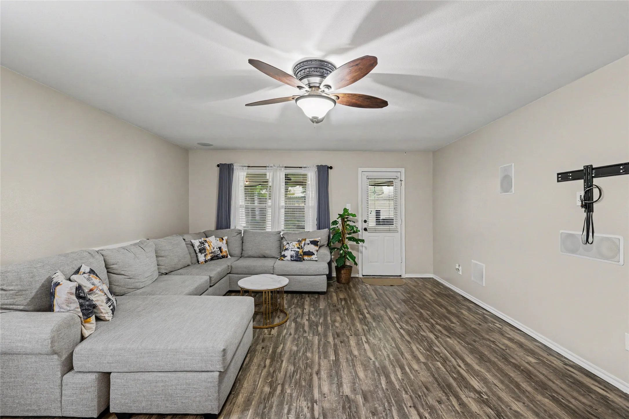 Spacious living area featuring wood-finish flooring, a ceiling fan, and recessed in-wall speakers