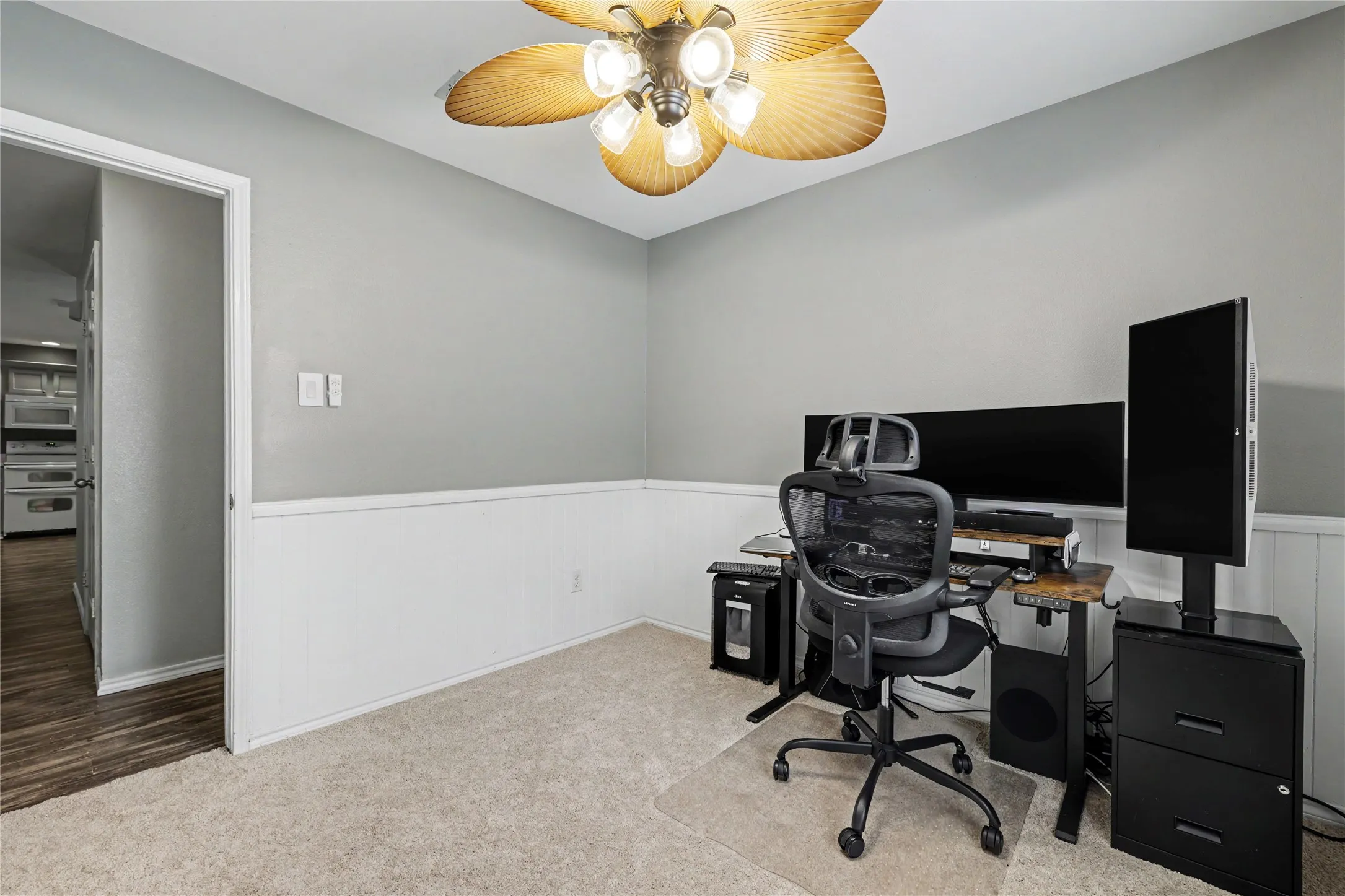 Carpeted room featuring a ceiling fan with integrated lighting, two-tone wall treatment, and a doorway opening to an area with wood-finish flooring