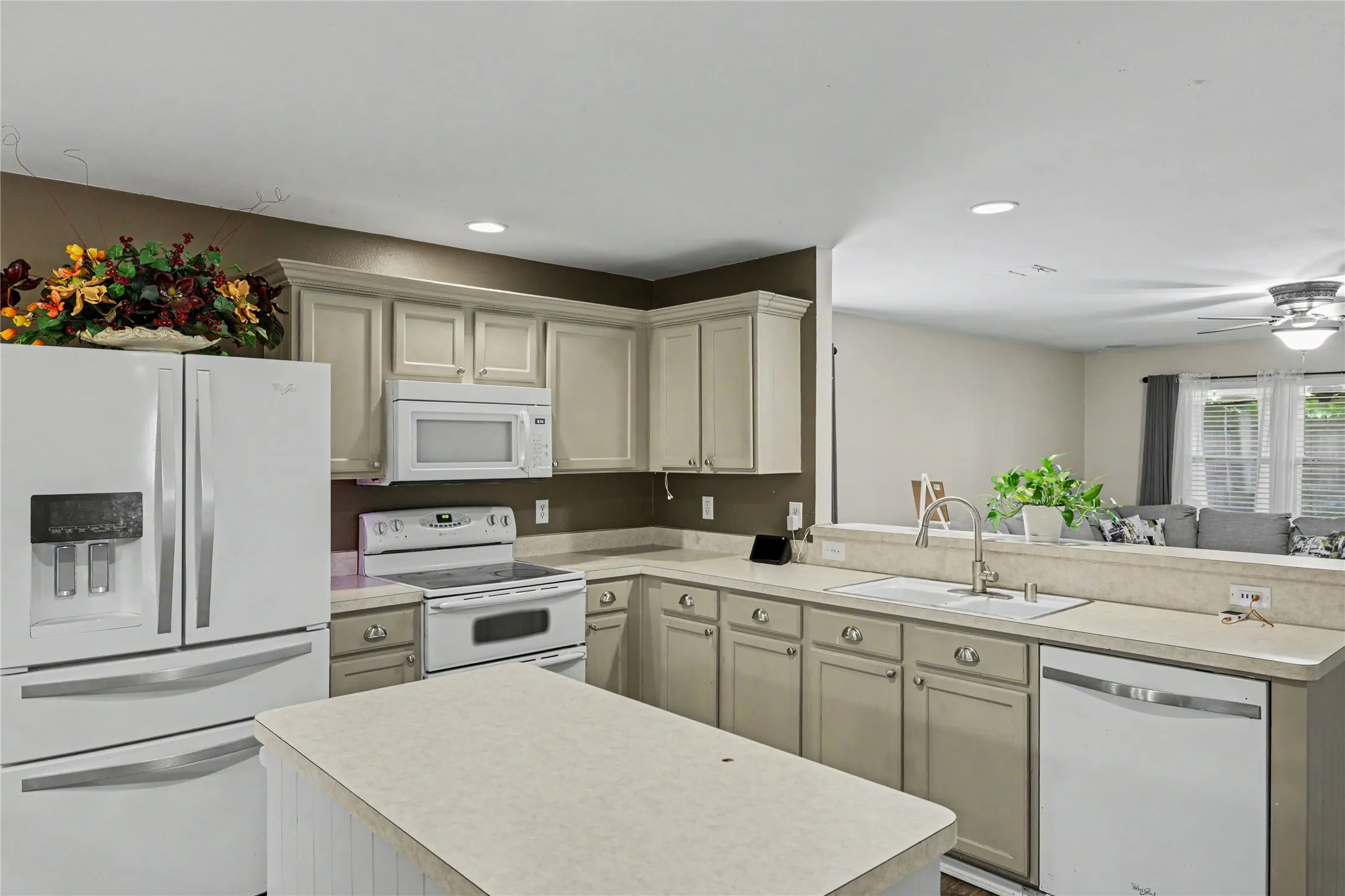 Kitchen featuring light-toned cabinetry, a central island, recessed lighting, and a pass-through opening to an adjacent living area