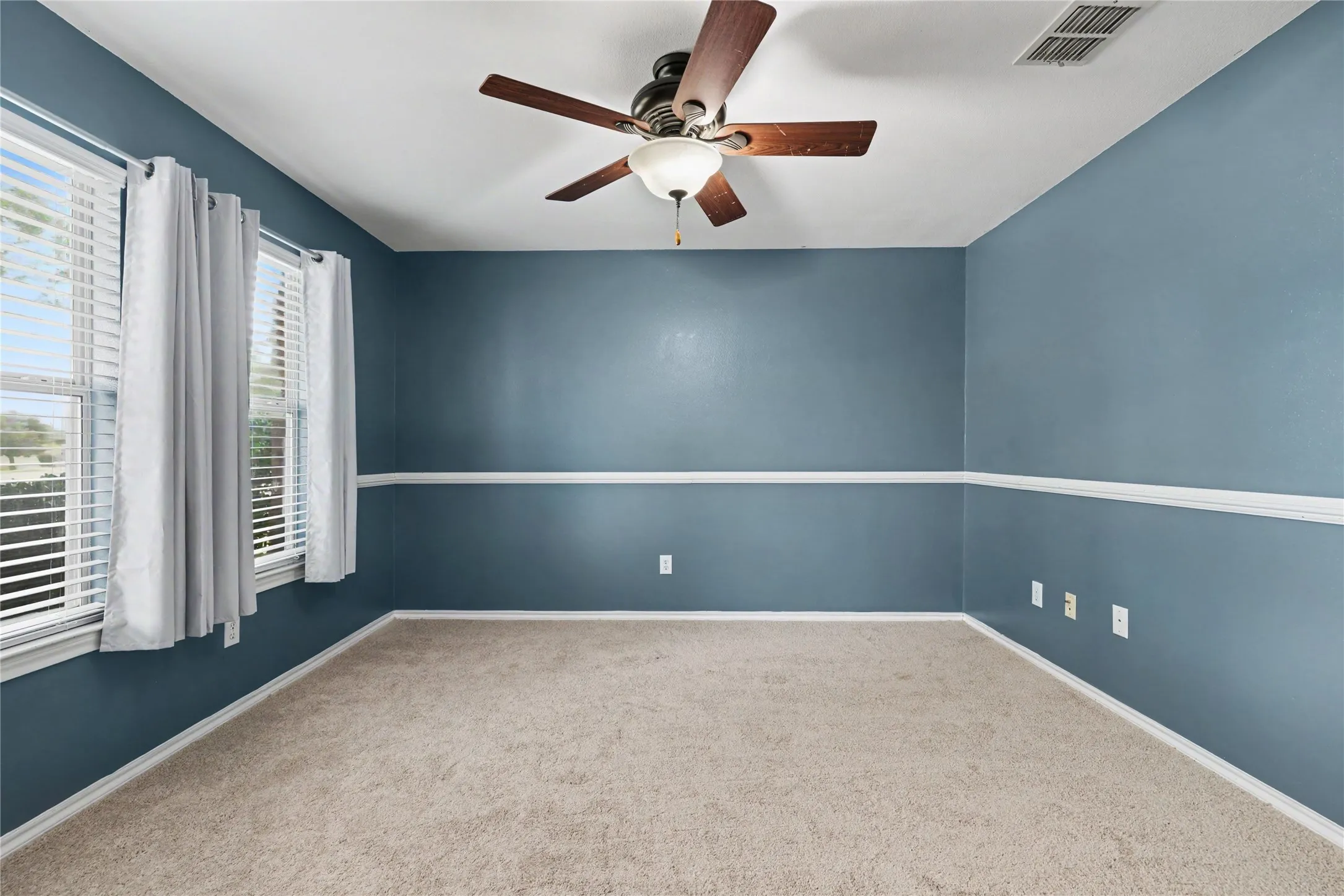 Room featuring plush carpeting, two windows with blinds, a ceiling fan with integrated lighting, and a white chair rail molding