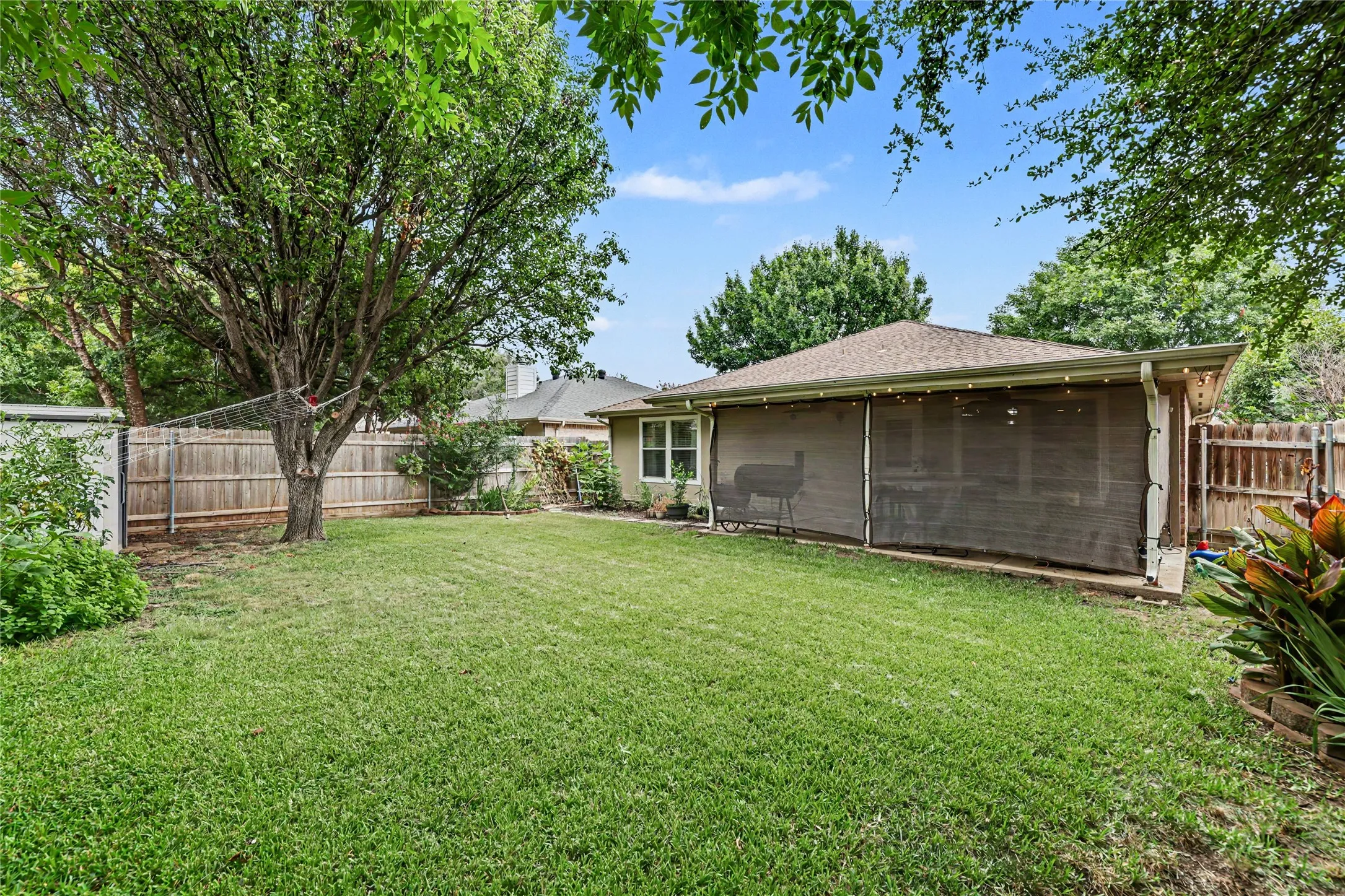 Expansive green lawn with mature trees and a wood privacy fence
