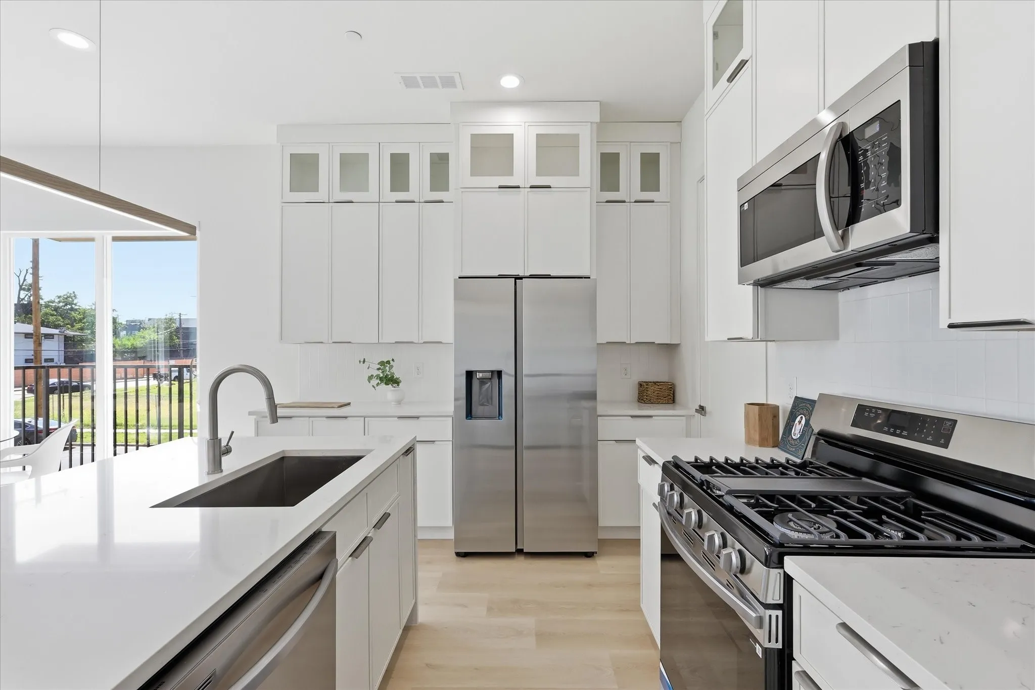Bright kitchen featuring extensive white cabinetry, stainless steel appliances, a large center island with an undermount sink, and wood-finish flooring