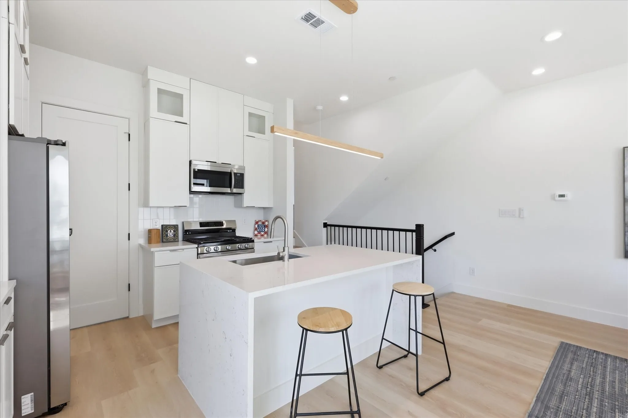 Modern kitchen featuring a central island with an integrated sink, white cabinetry, stainless steel appliances, and wood-finish flooring