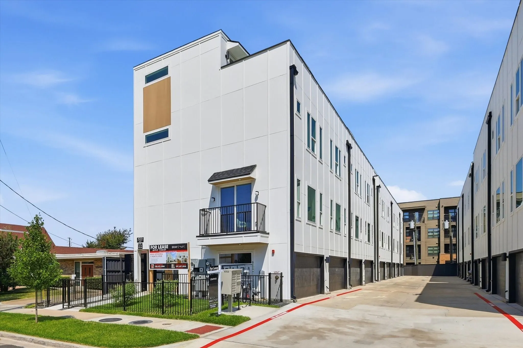Modern multi-story townhouse exterior featuring white panel siding, a private balcony with black iron railing, and dark-framed windows