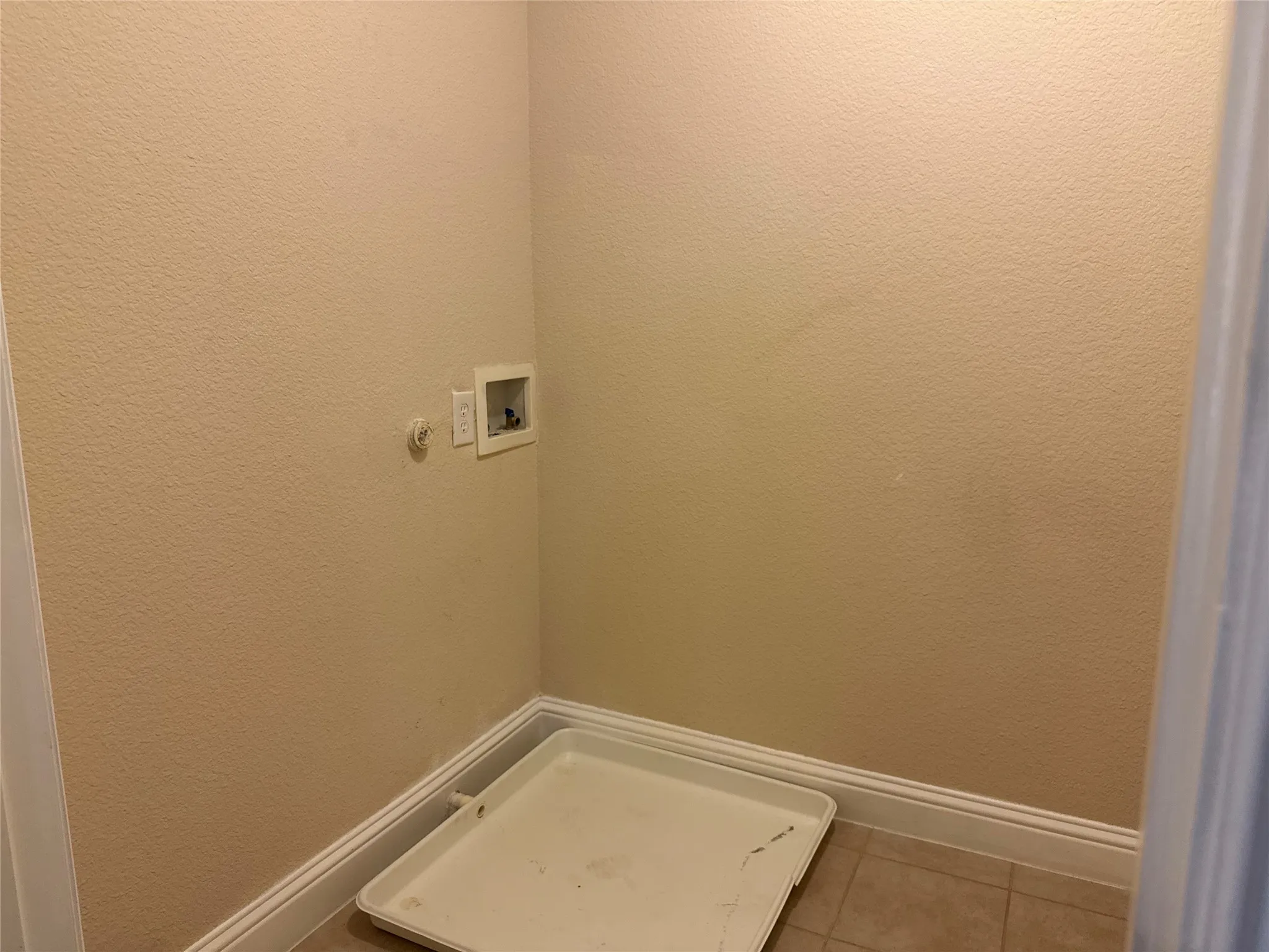 Dedicated utility space with textured walls, tile flooring, and essential hookups