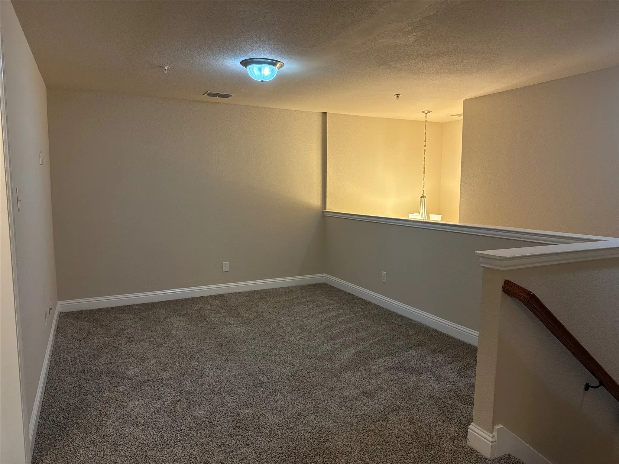 Carpeted loft area featuring a partial wall opening to a lower level, a wooden handrail, and baseboard molding