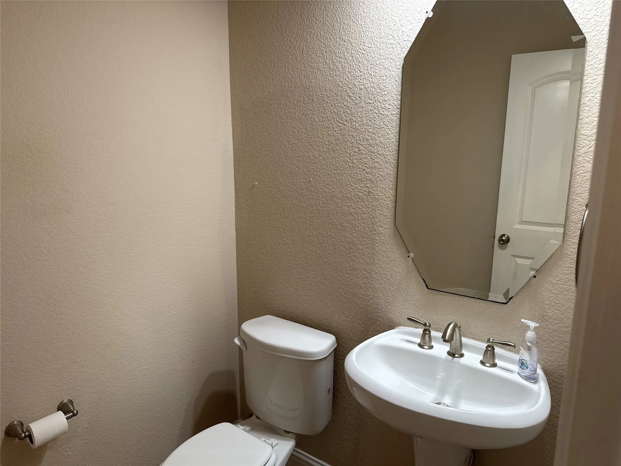 Pedestal sink with a brushed nickel faucet and an octagonal frameless mirror