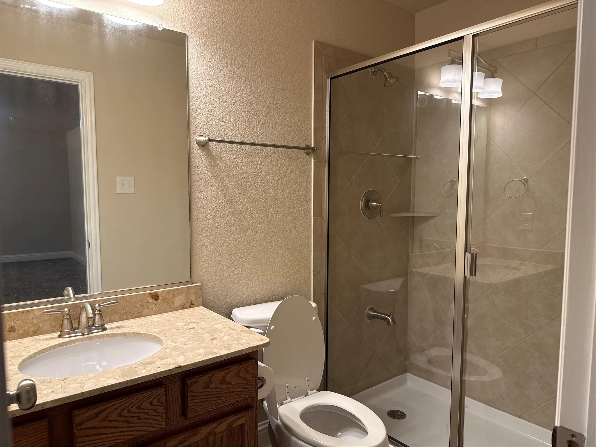Shower with glass enclosure, integrated tile shelving, and a vanity featuring an undermount sink with a stone countertop