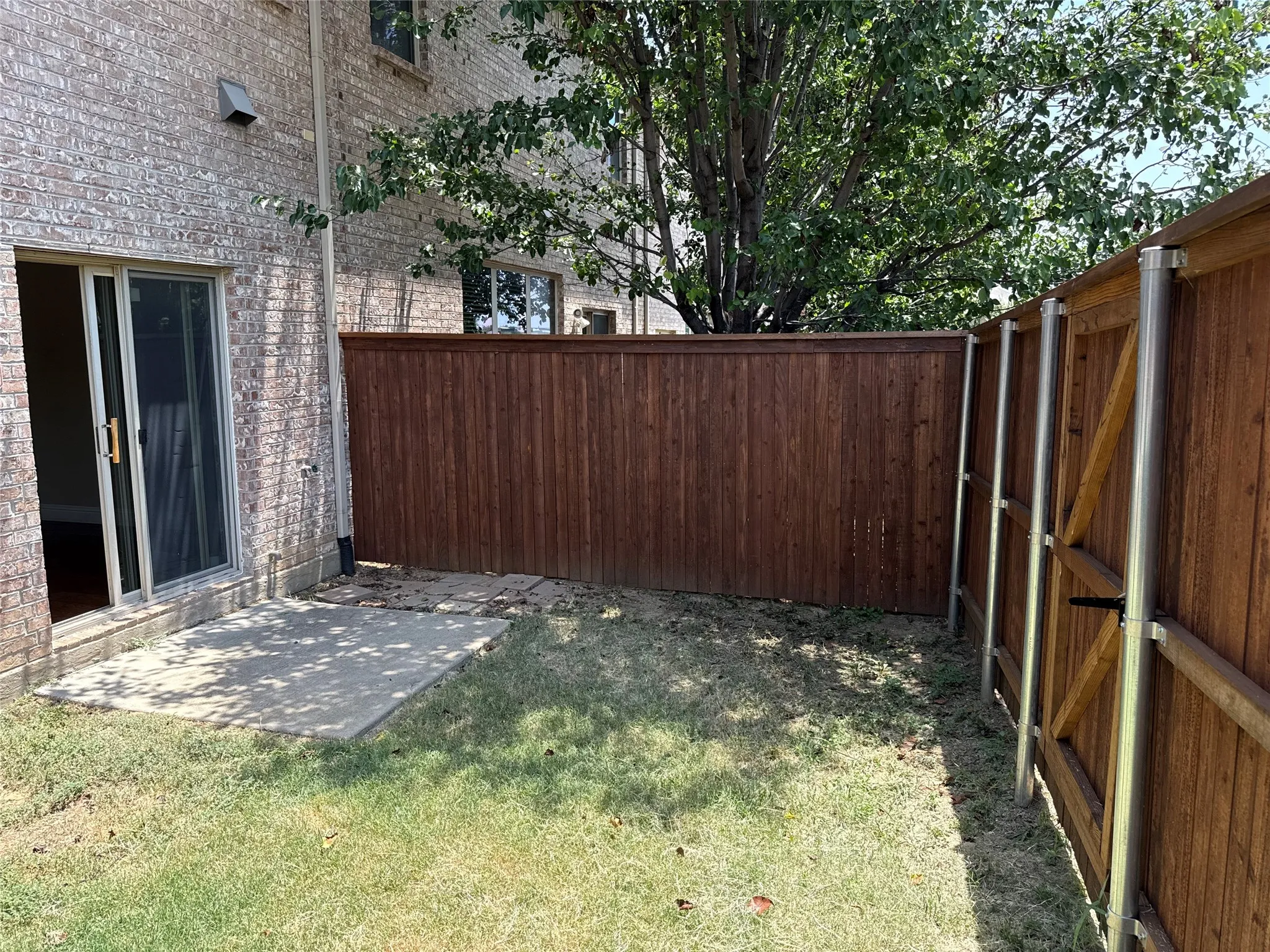 Private yard space featuring a wood fence, concrete patio, and brick exterior