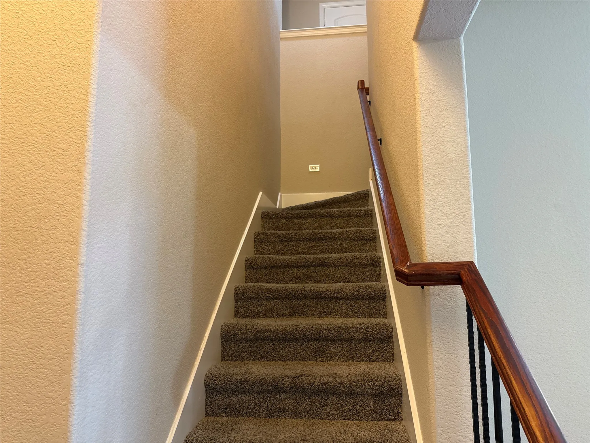 Carpeted staircase featuring a dark wood-finish handrail and wrought iron balusters