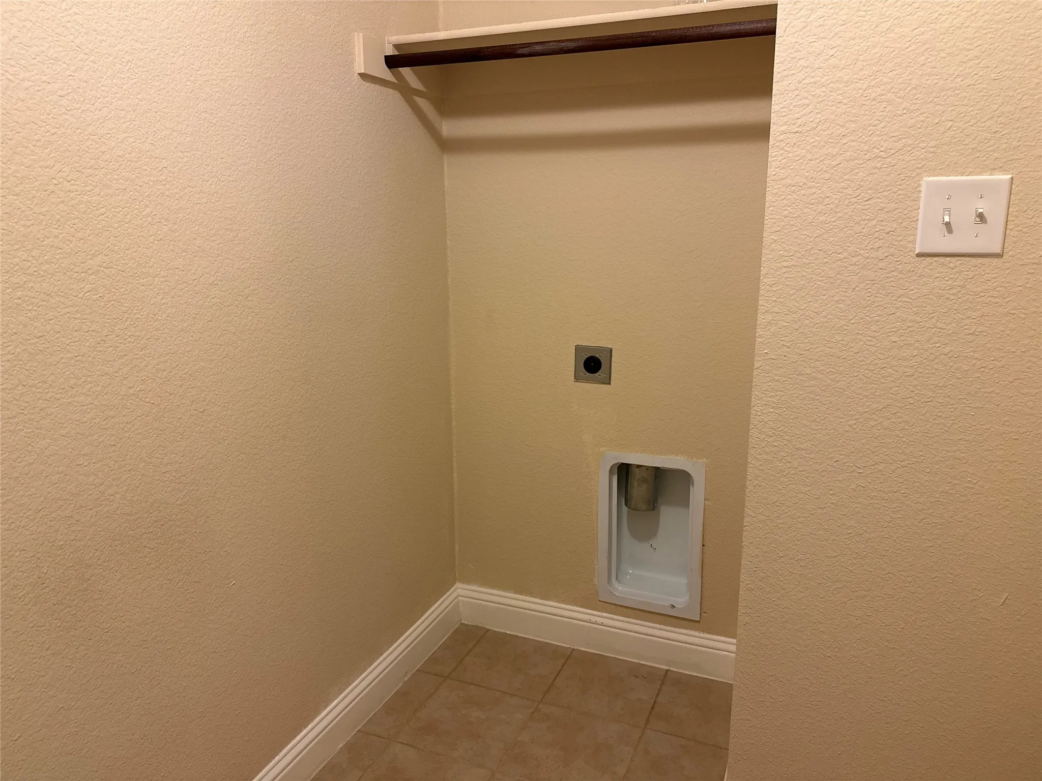 Dedicated utility alcove featuring tile flooring, a wall-mounted shelf, and a clothing rod