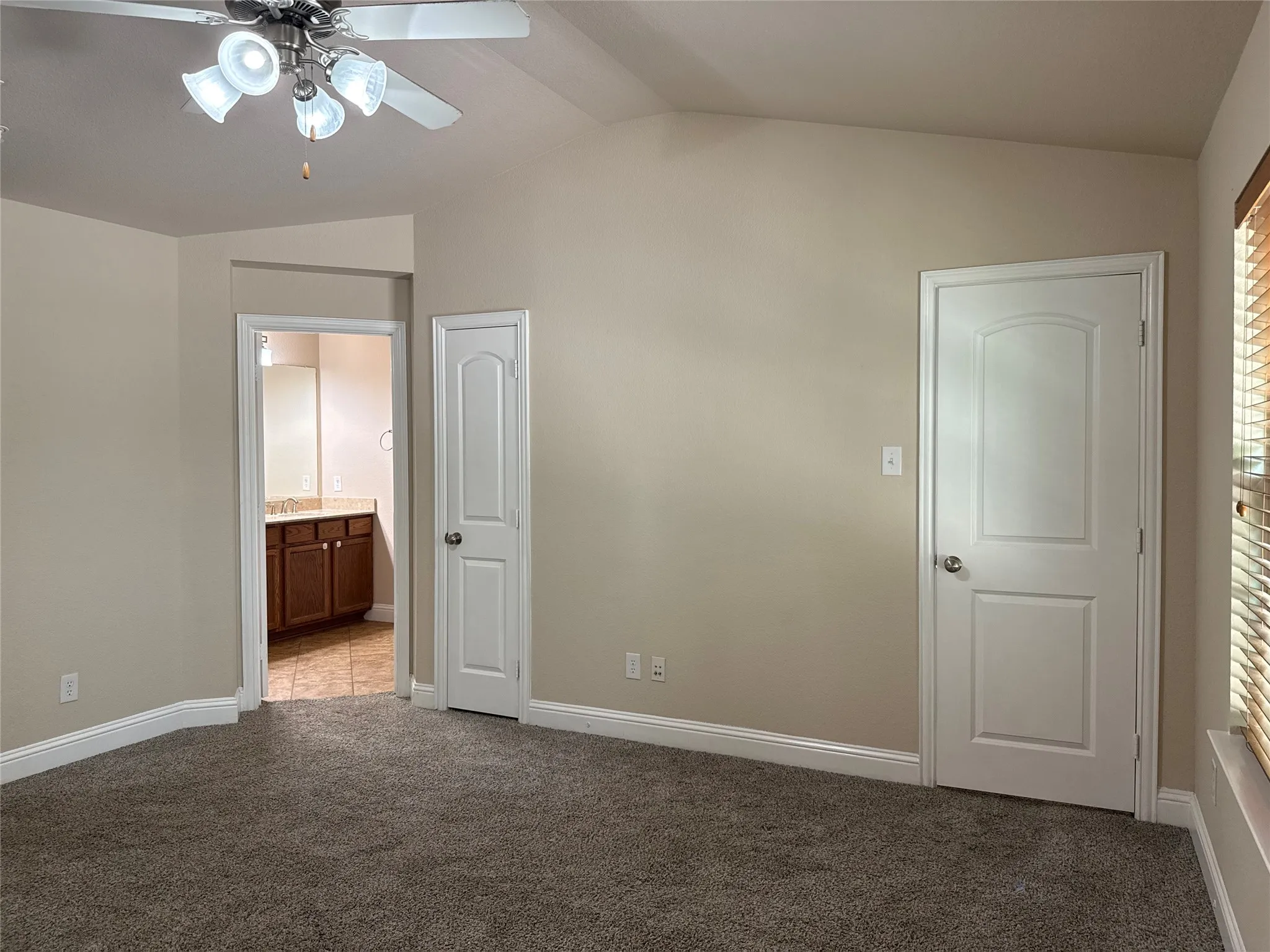 Carpeted room featuring a vaulted ceiling and a ceiling fan with integrated lighting