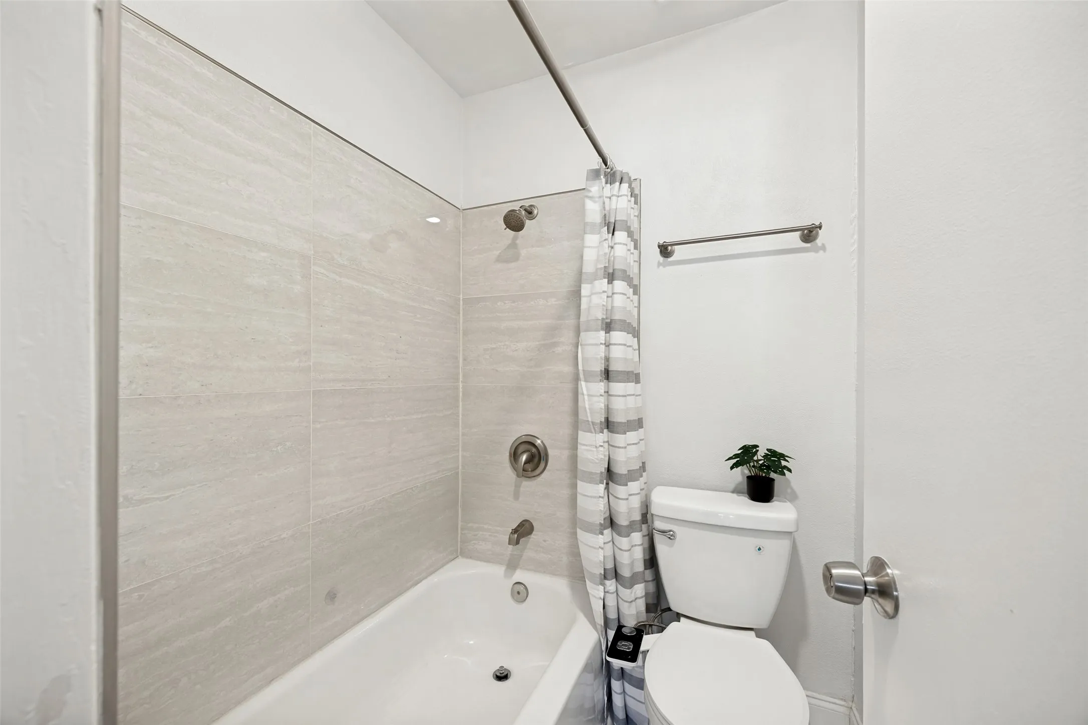 Tub and shower combination featuring light-toned large format tile surround and brushed nickel fixtures