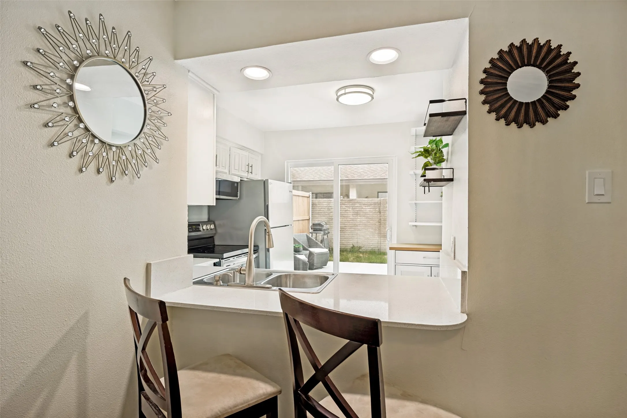 Bright kitchen pass-through featuring a peninsula countertop, stainless steel sink with a gooseneck faucet, white cabinetry, and recessed lighting