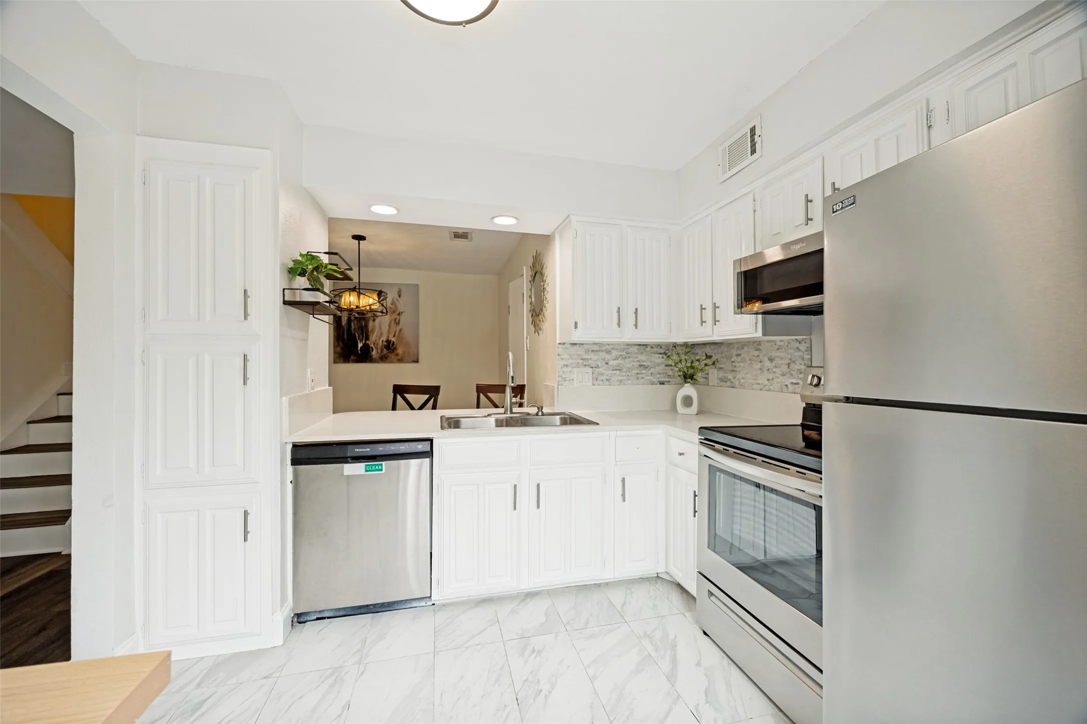 Bright kitchen featuring white cabinetry, stainless steel appliances, a white tile backsplash, light-toned countertops, and a pass-through opening