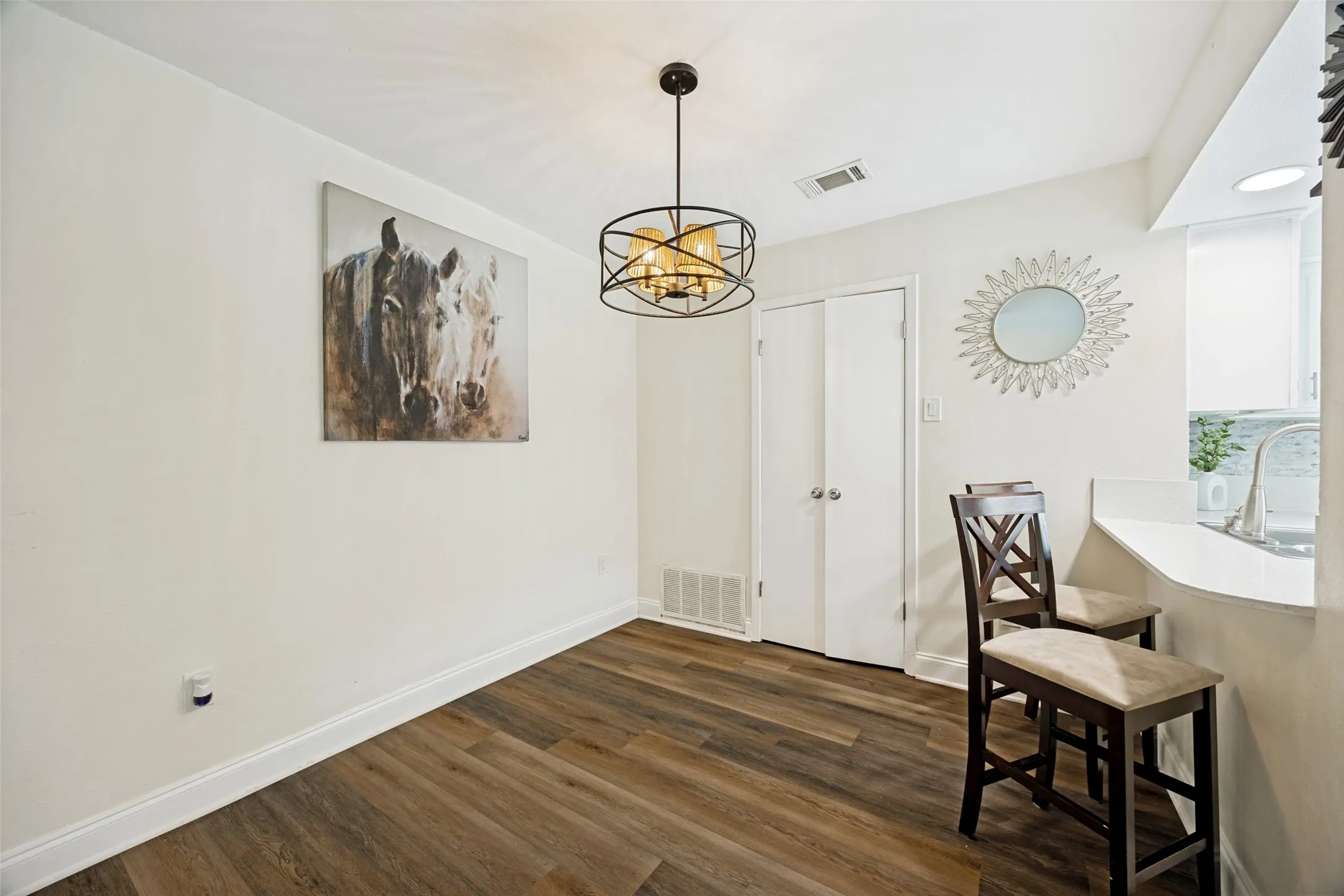 Dining area featuring wood-finish flooring, a contemporary chandelier, white baseboards, and a pass-through counter with seating