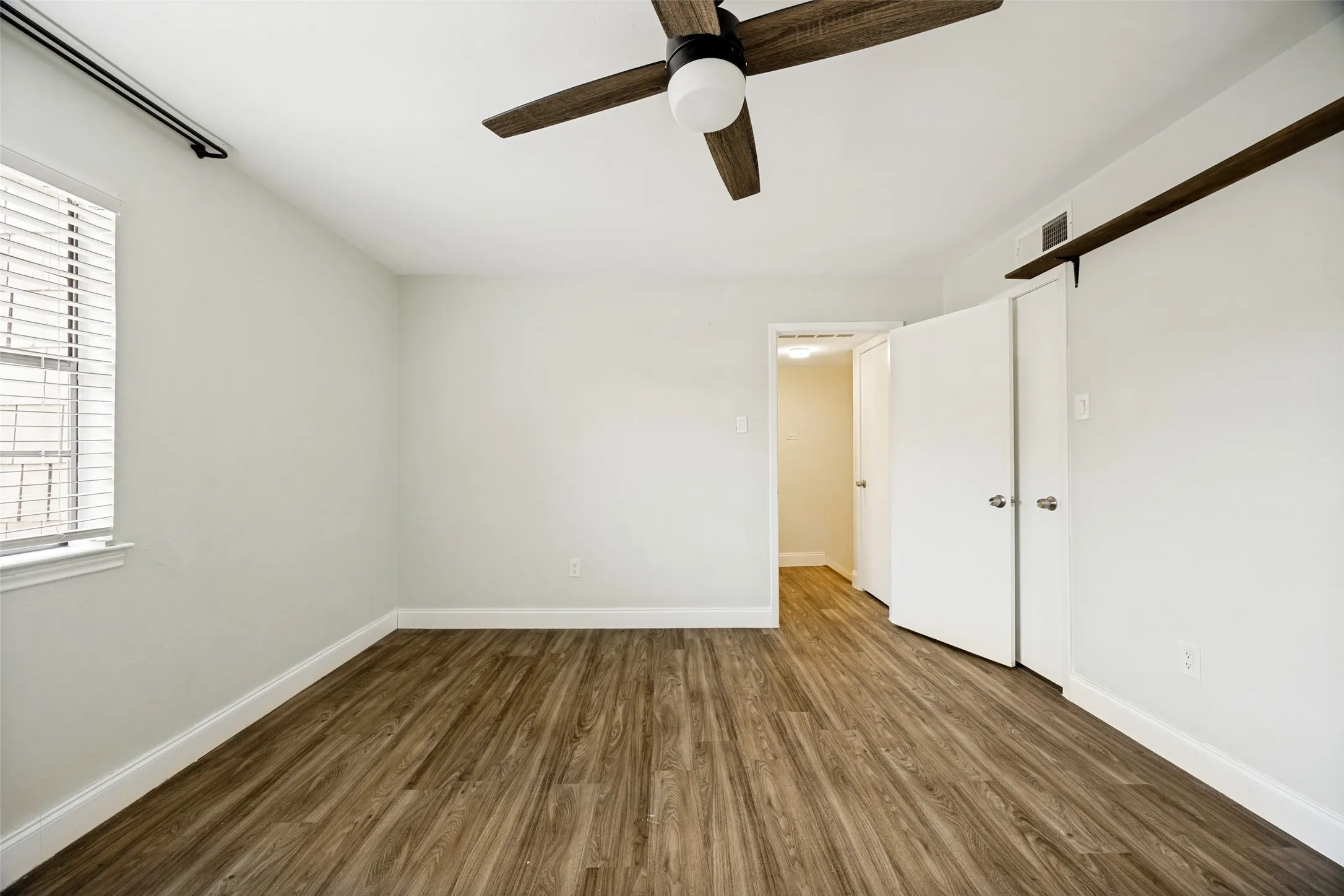 Spacious room featuring wood-finish flooring, light-toned walls, and a ceiling fan with integrated lighting