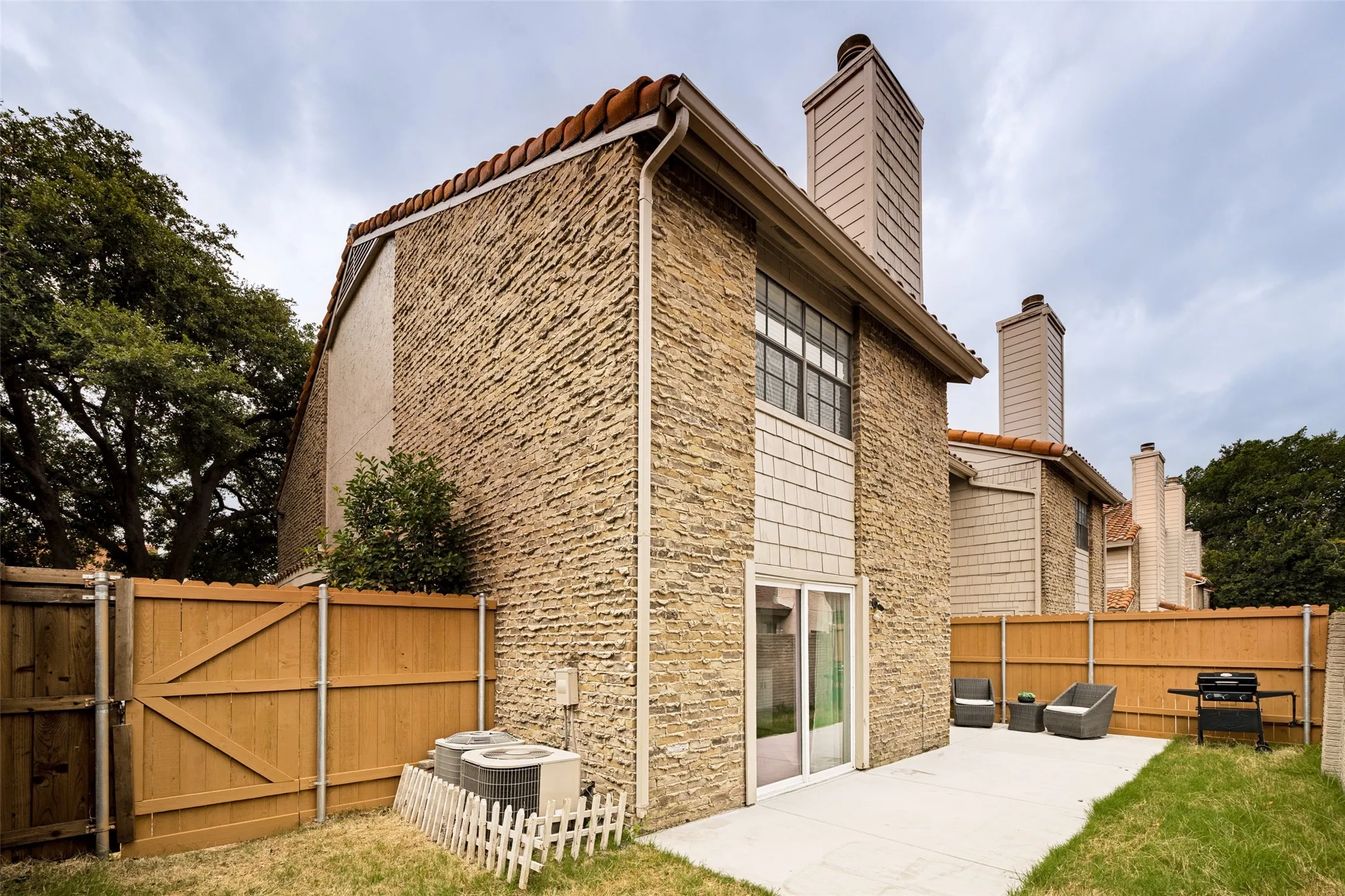 Rear exterior featuring stone veneer siding, terra cotta roof tiles, and a private fenced yard