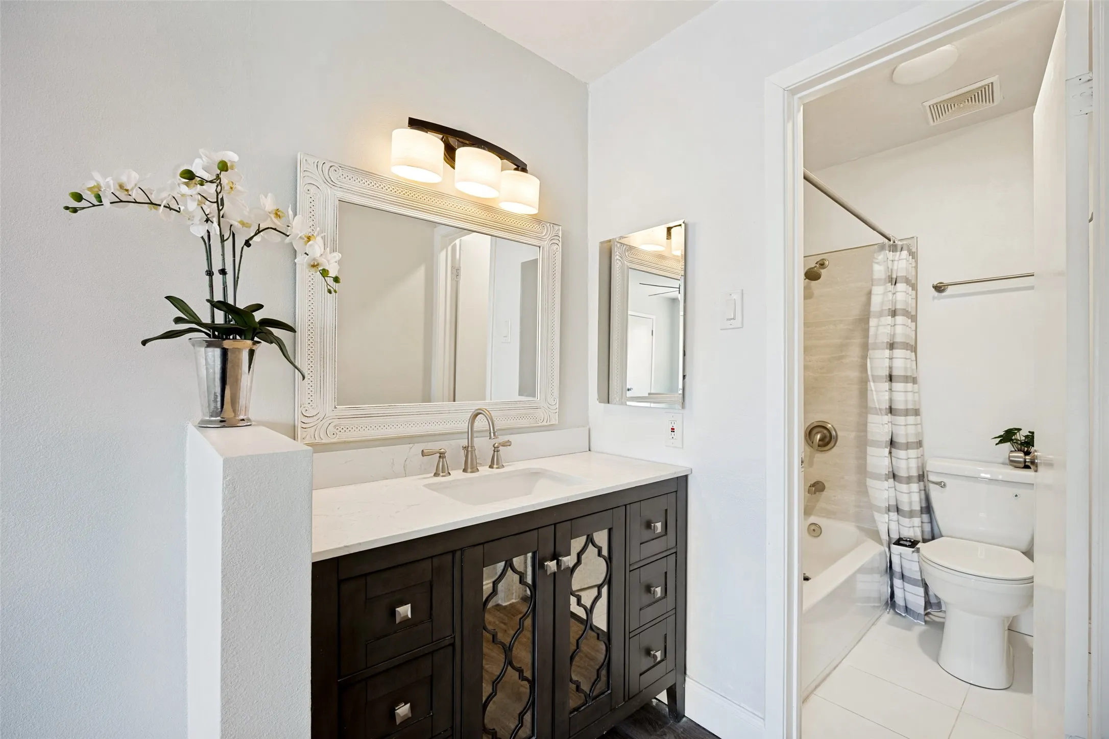 Bathroom vanity featuring a white countertop, undermount sink, brushed nickel faucet, and a dark wood-finish cabinet with decorative mirror panels
