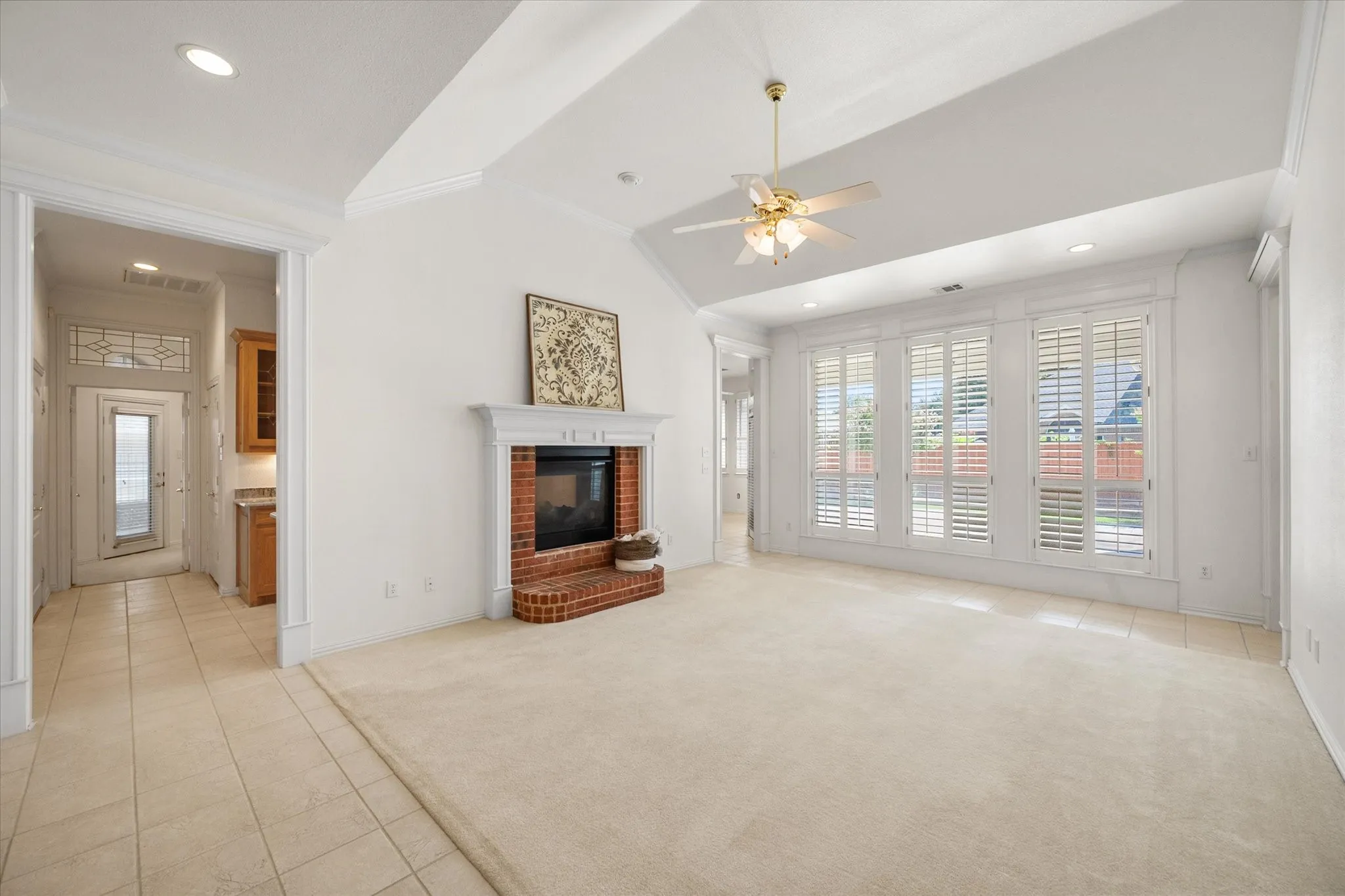 Formal living room has a fireplace, plantation shutters and overlooks the backyard.