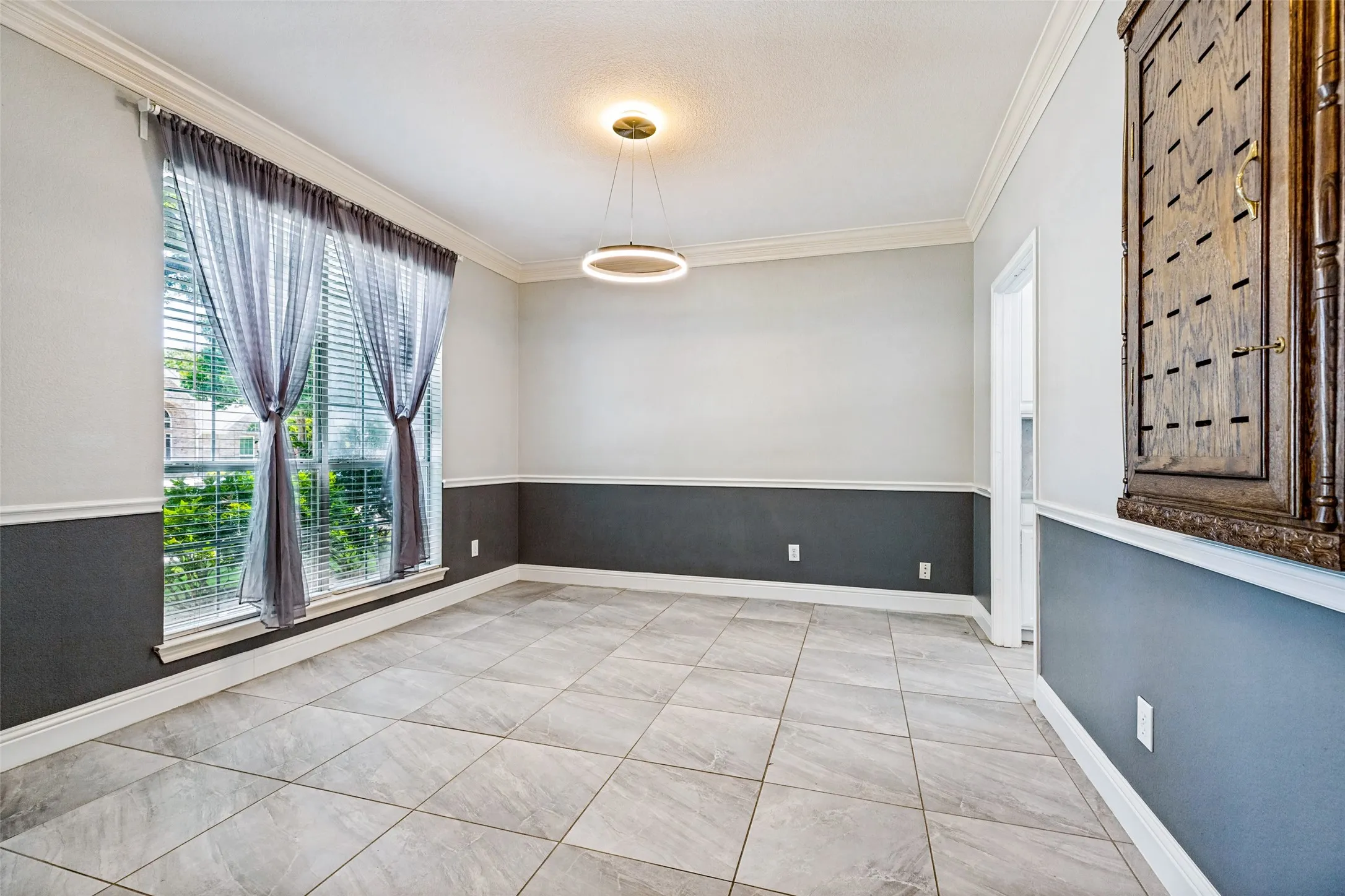 Neutral-toned large format tile flooring complements the two-tone wall treatment with chair rail molding
