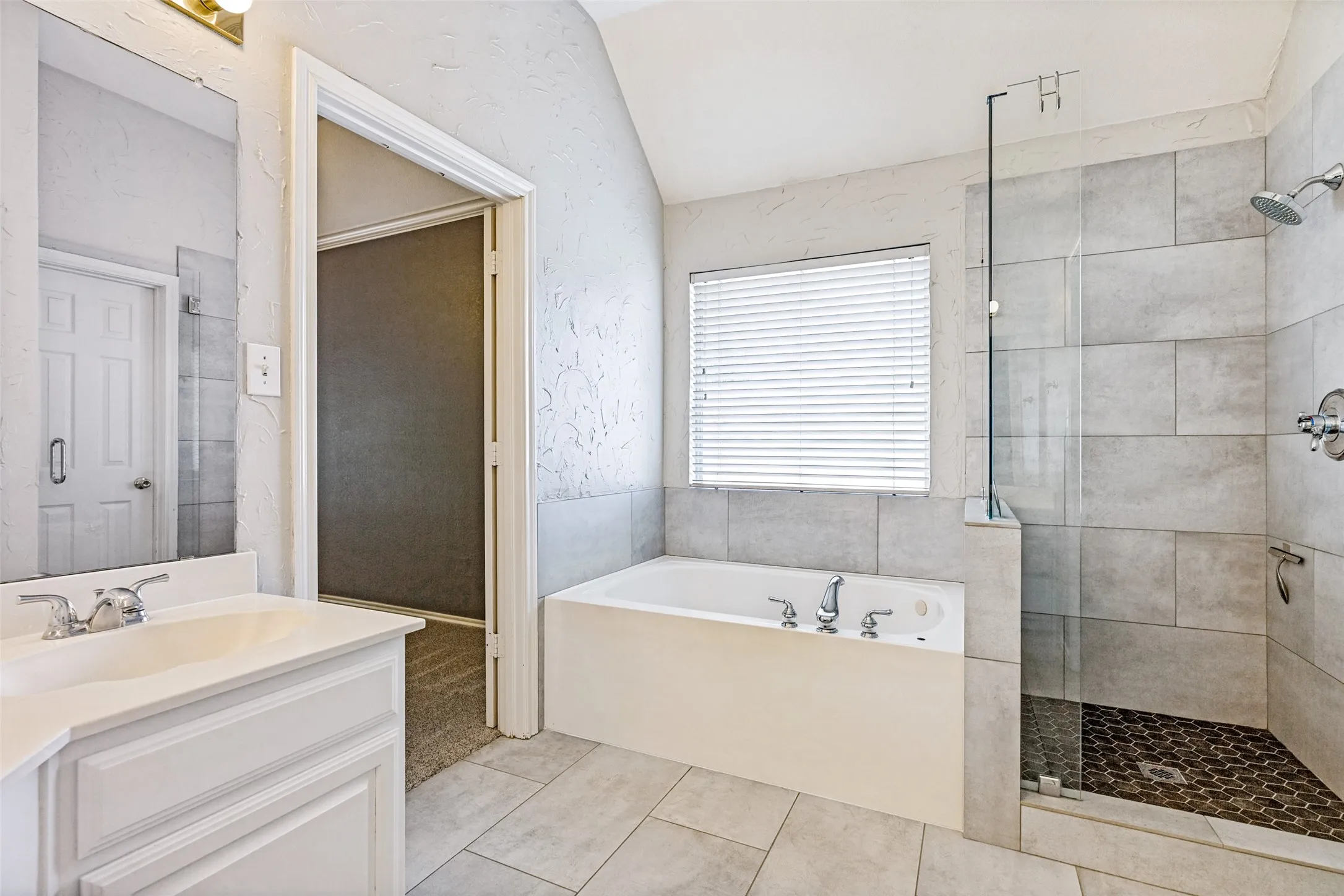White soaking tub with chrome fixtures, a tiled shower with glass enclosure, and a single vanity with a white countertop and chrome faucet