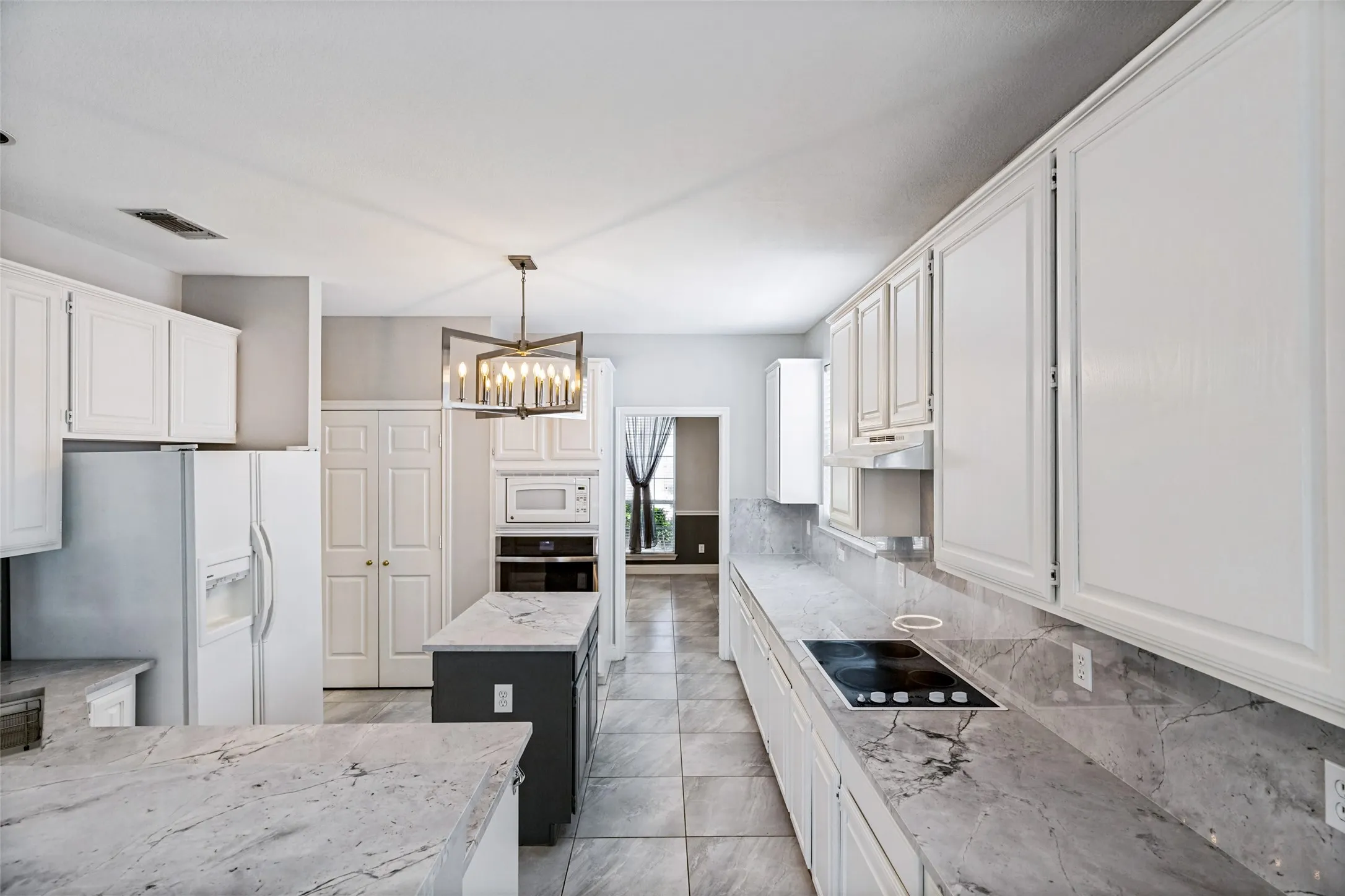 Kitchen featuring a central island with a dark base, light-toned countertops, white cabinetry, a built-in cooktop, and tile flooring